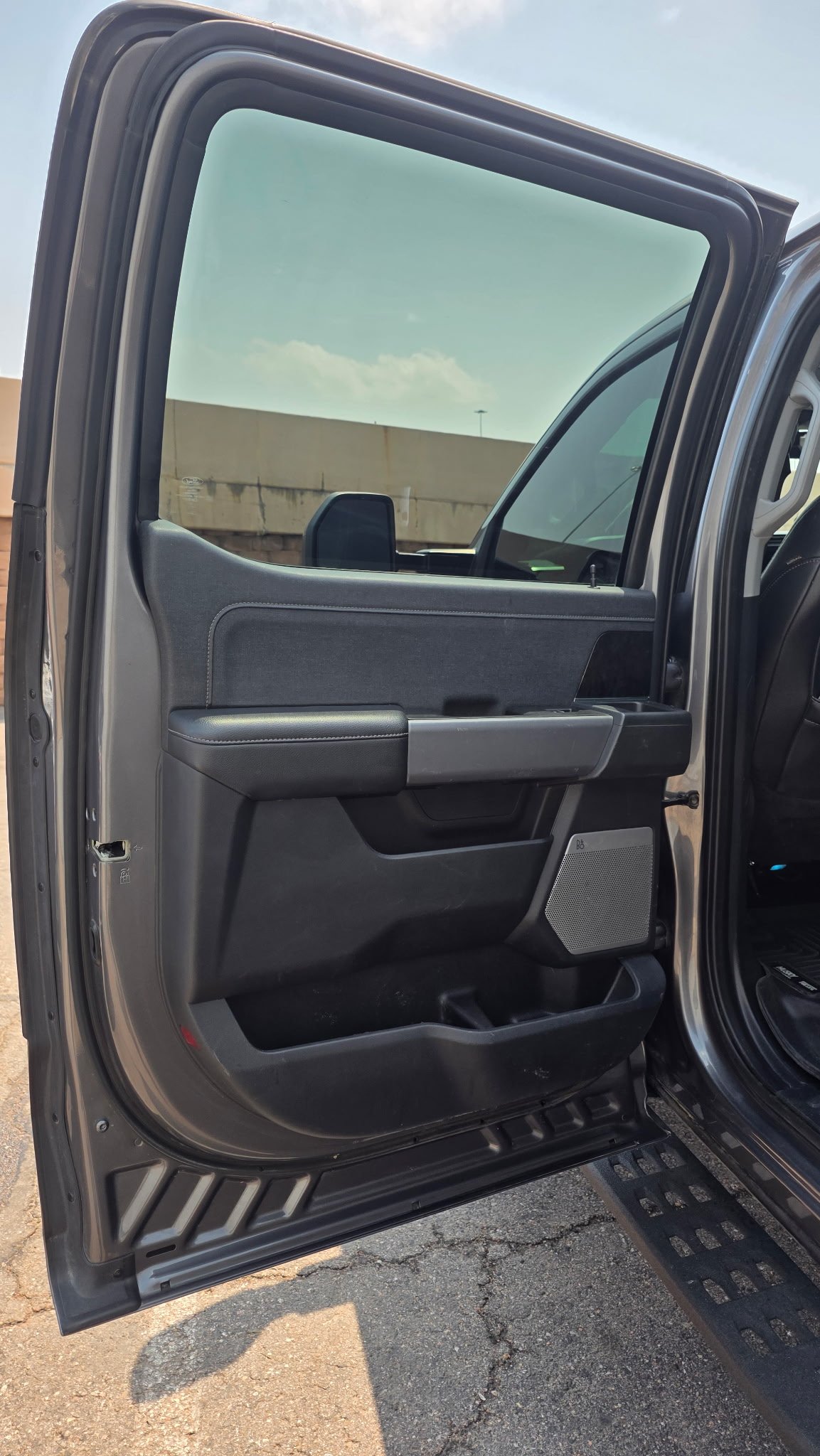 Open truck door showing the interior panel, window, and side mirror with a highway wall and sky in the background.