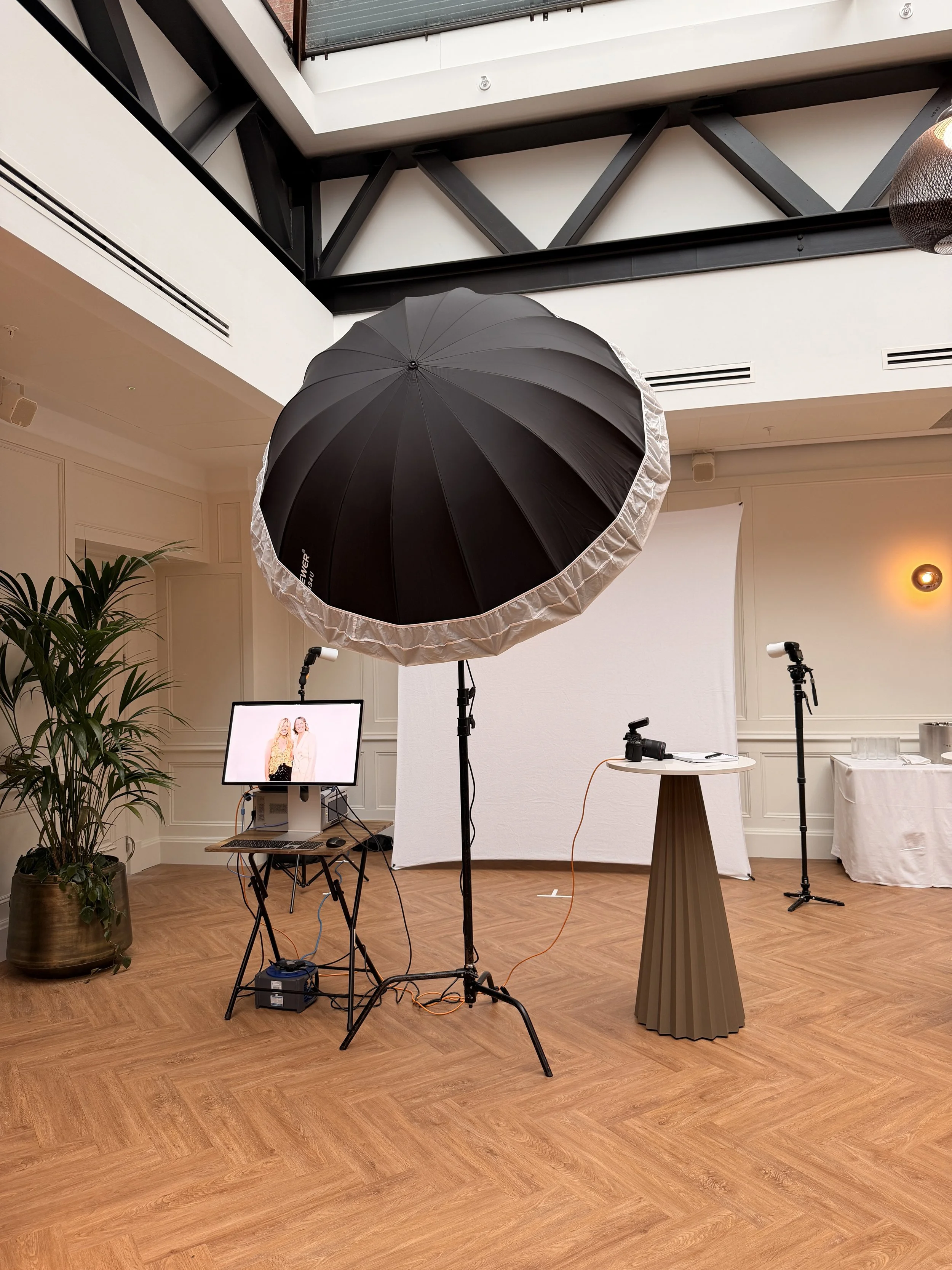 Photography studio setup with large umbrella light, camera, and backdrop in an indoor space.