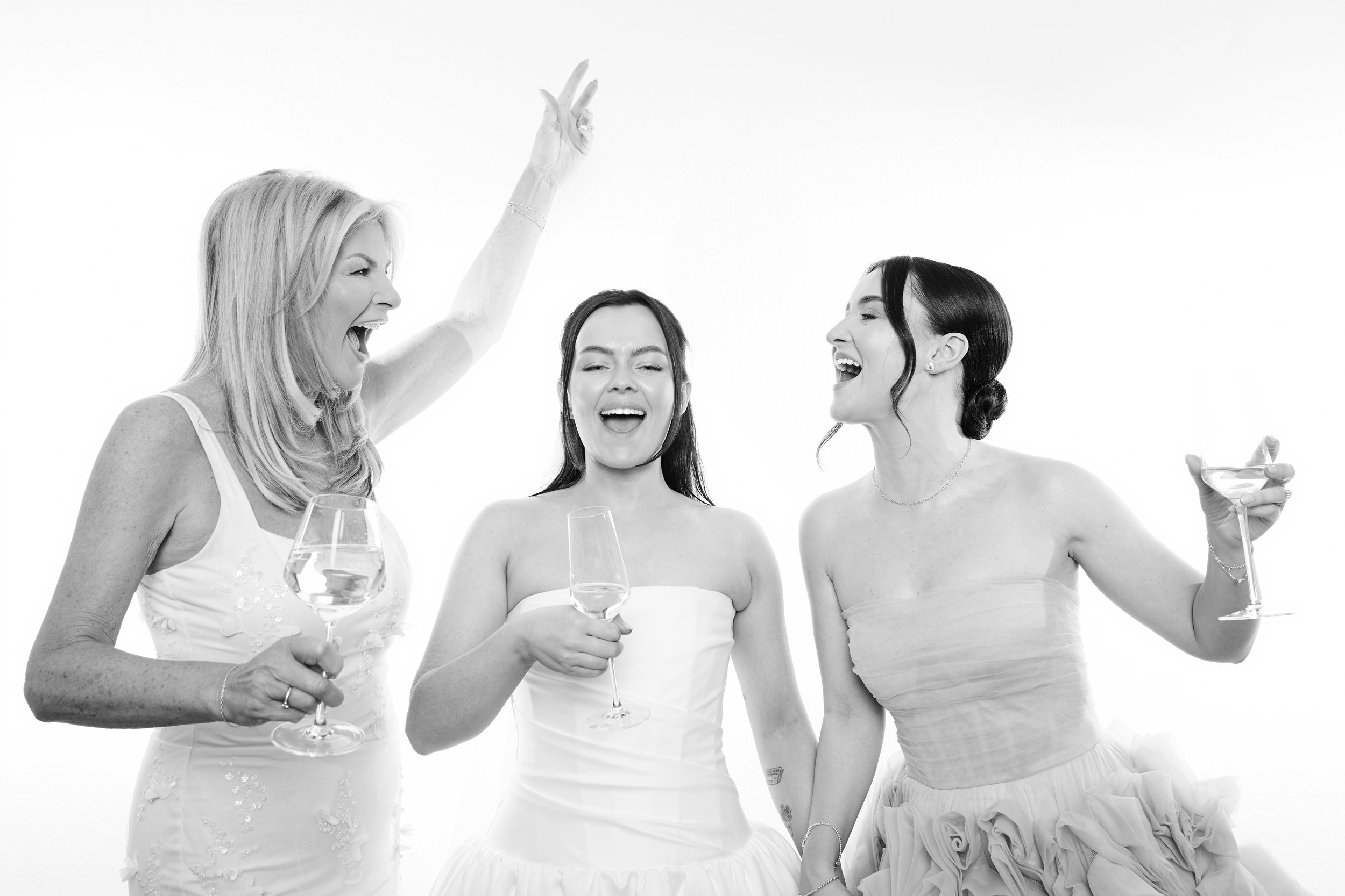 Four women dressed in white, holding wine glasses, smiling and talking to each other.