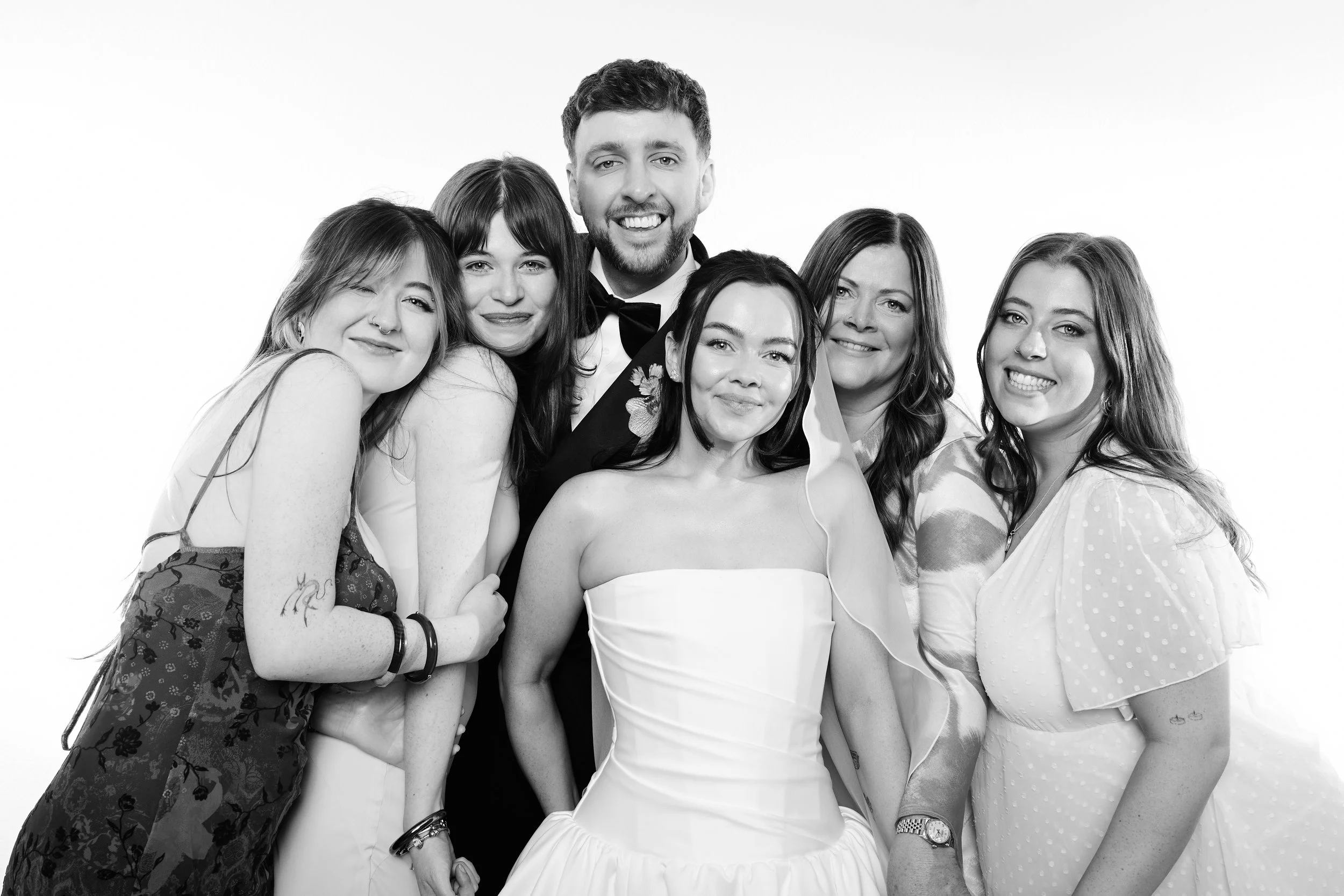 A group of six people at a formal event, with one woman wearing a wedding dress, smiling for the camera in a black-and-white photograph.