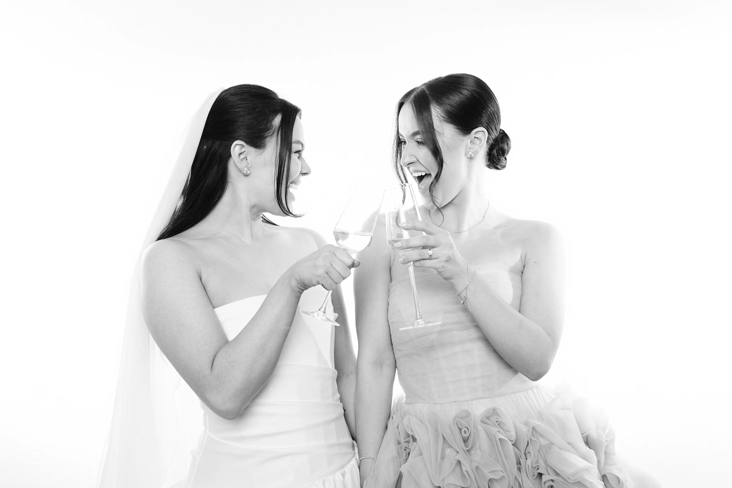 Two women dressed as brides smiling and toasting with glasses of champagne.