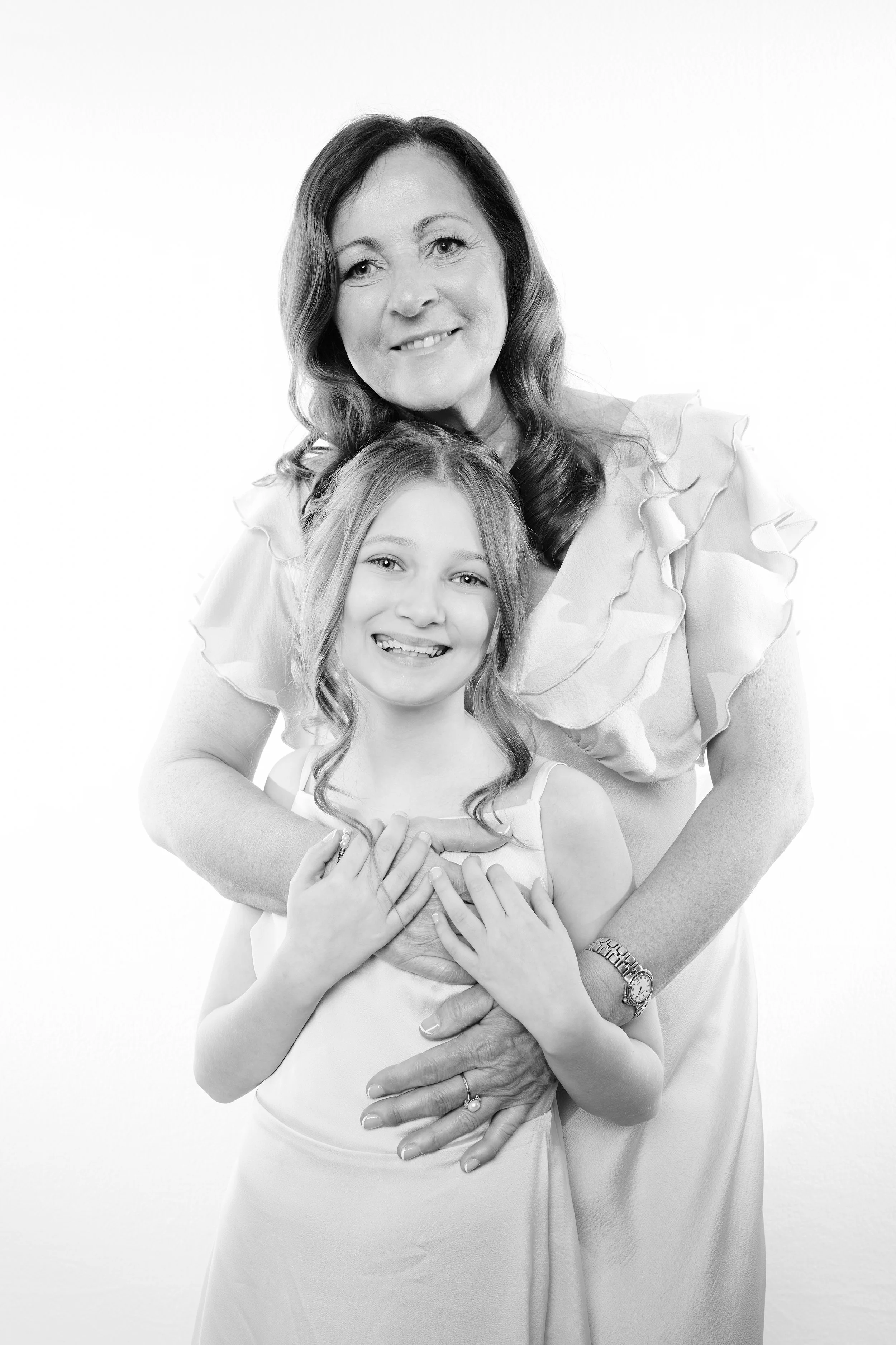 A woman and a young girl smiling and embracing in a close-up black and white portrait.