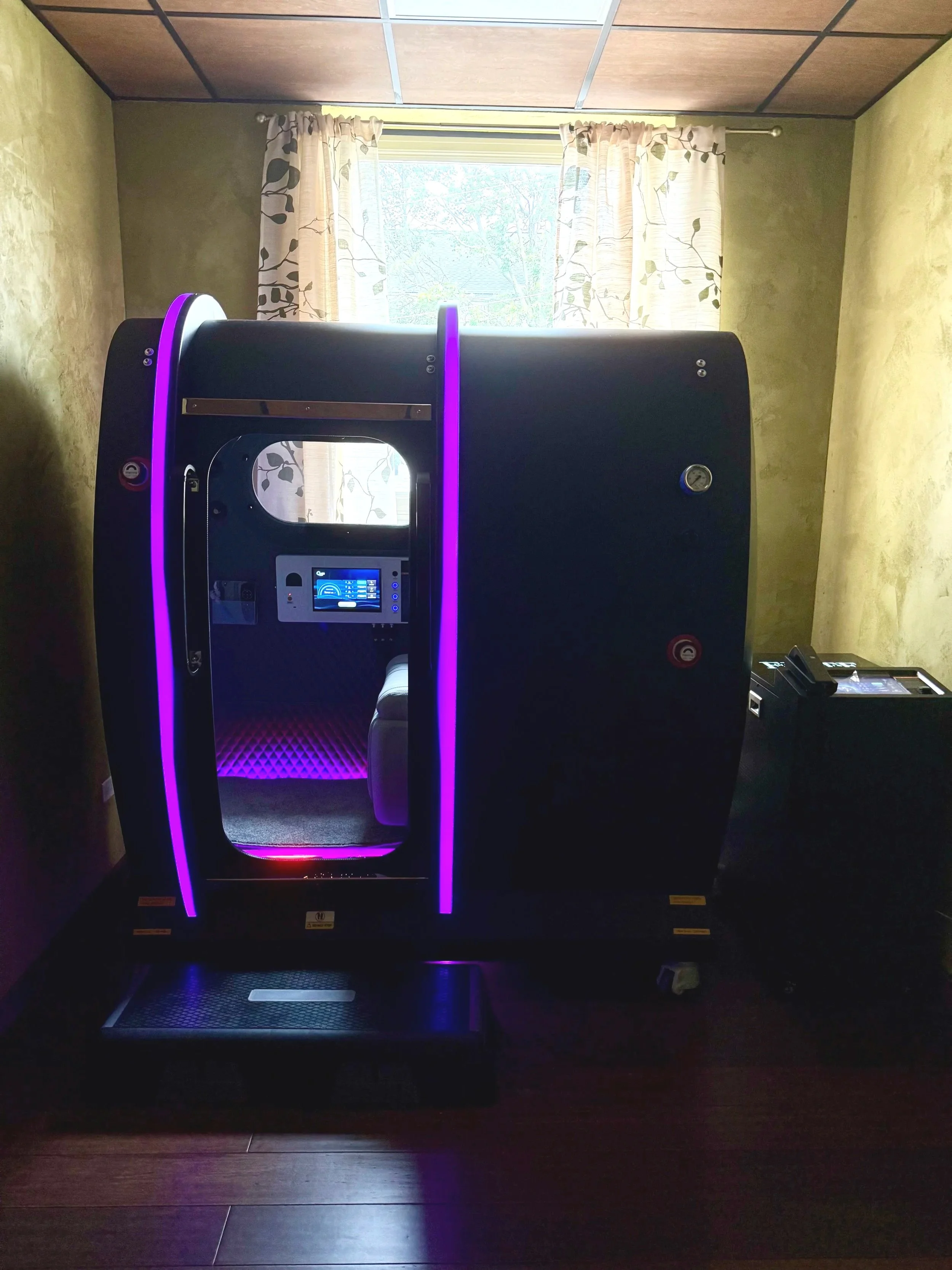 A black machine with purple LED lights inside a room with yellow walls and a window with floral curtains.