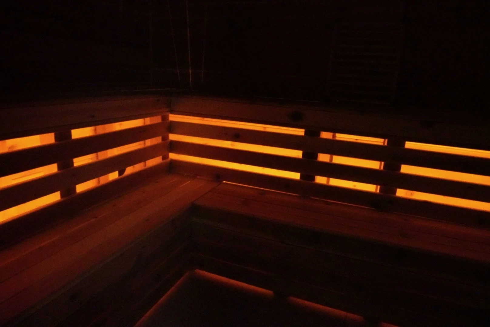 Dimly lit wooden sauna with horizontal slats and internal lighting along the edges.