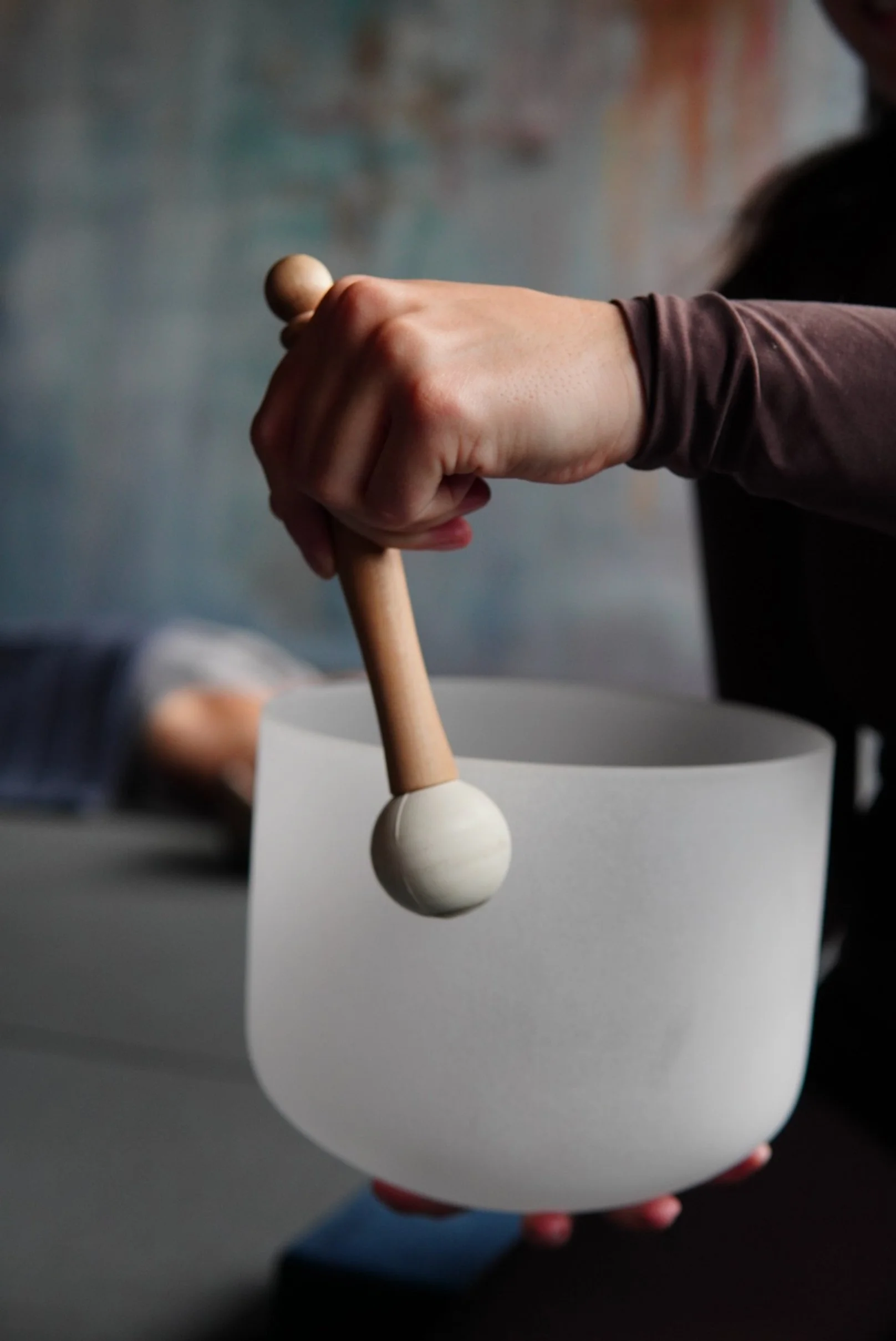 A person using a wooden mallet to strike a white singing bowl.