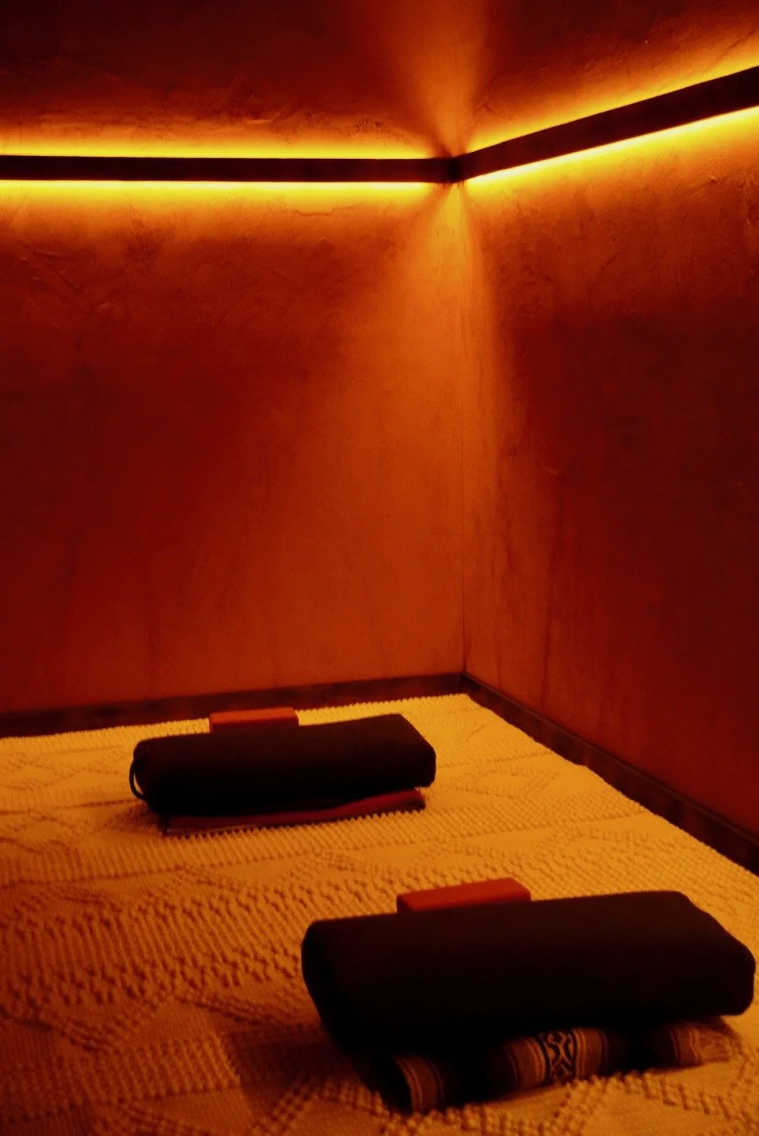 Dimly lit room with orange lighting, two black rolled towels on a textured yellow mat, and bamboo mats underneath the towels.