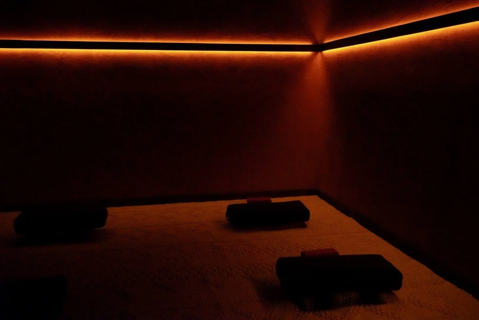 Dark room with warm orange lighting along the ceiling and walls, and objects on a textured surface.