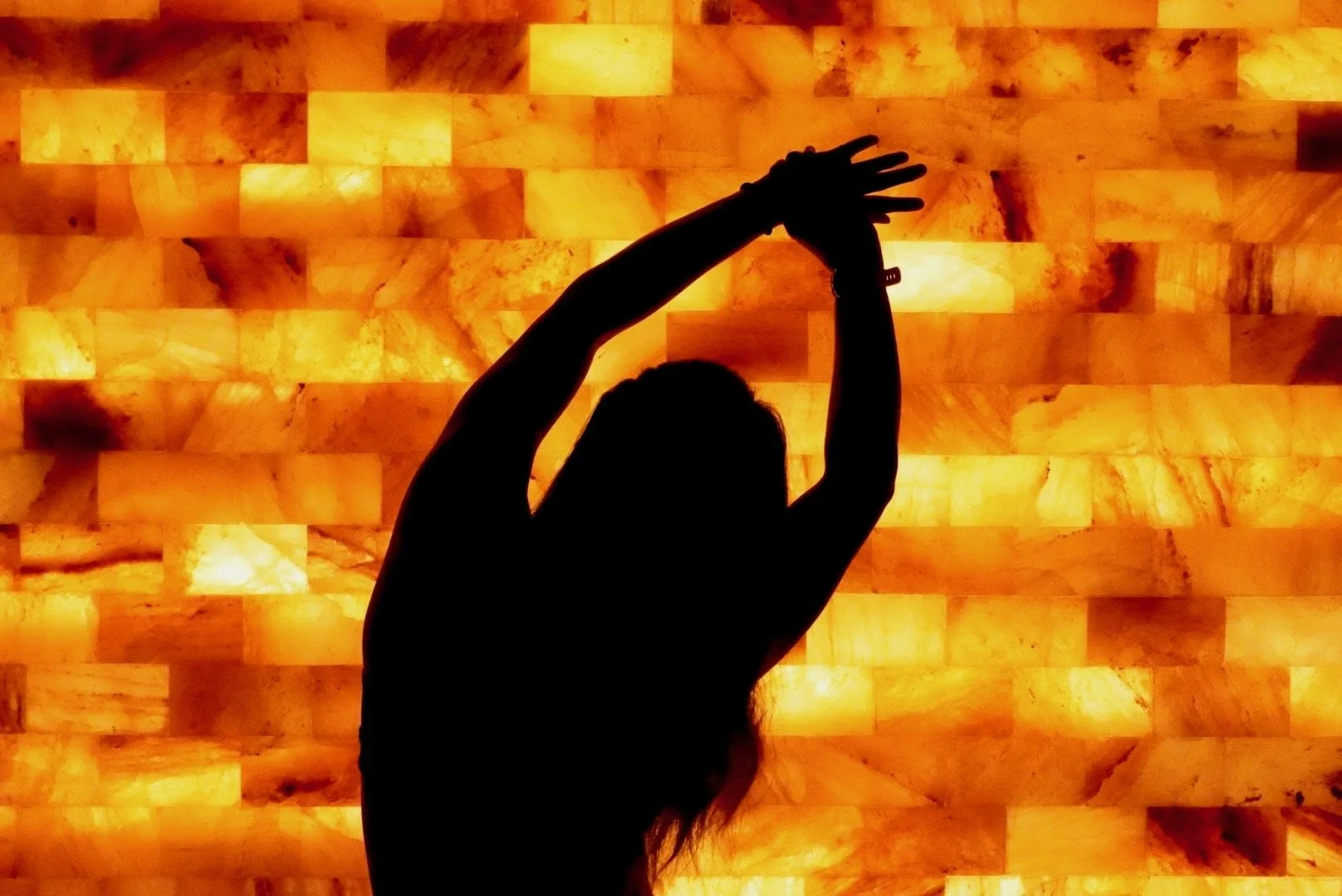 Silhouette of a person stretching in front of a backlit salt wall.