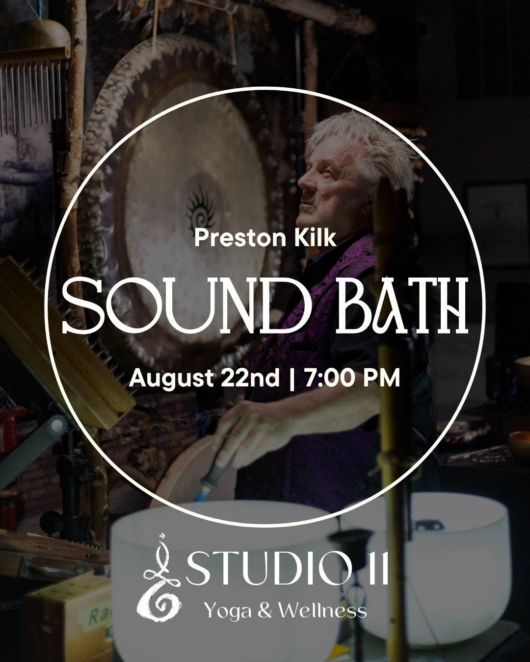A person playing a sound bath gong surrounded by singing bowls and musical instruments in a dimly lit room.