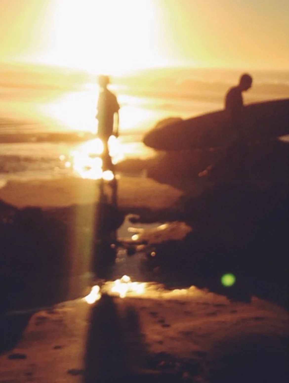 Two people standing outdoors near water during sunset, with one person in the foreground and the other in the background.