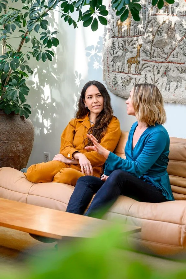Two women sitting in conversation on a sofa in a light-filled therapy space. #slideInLeft-scroll