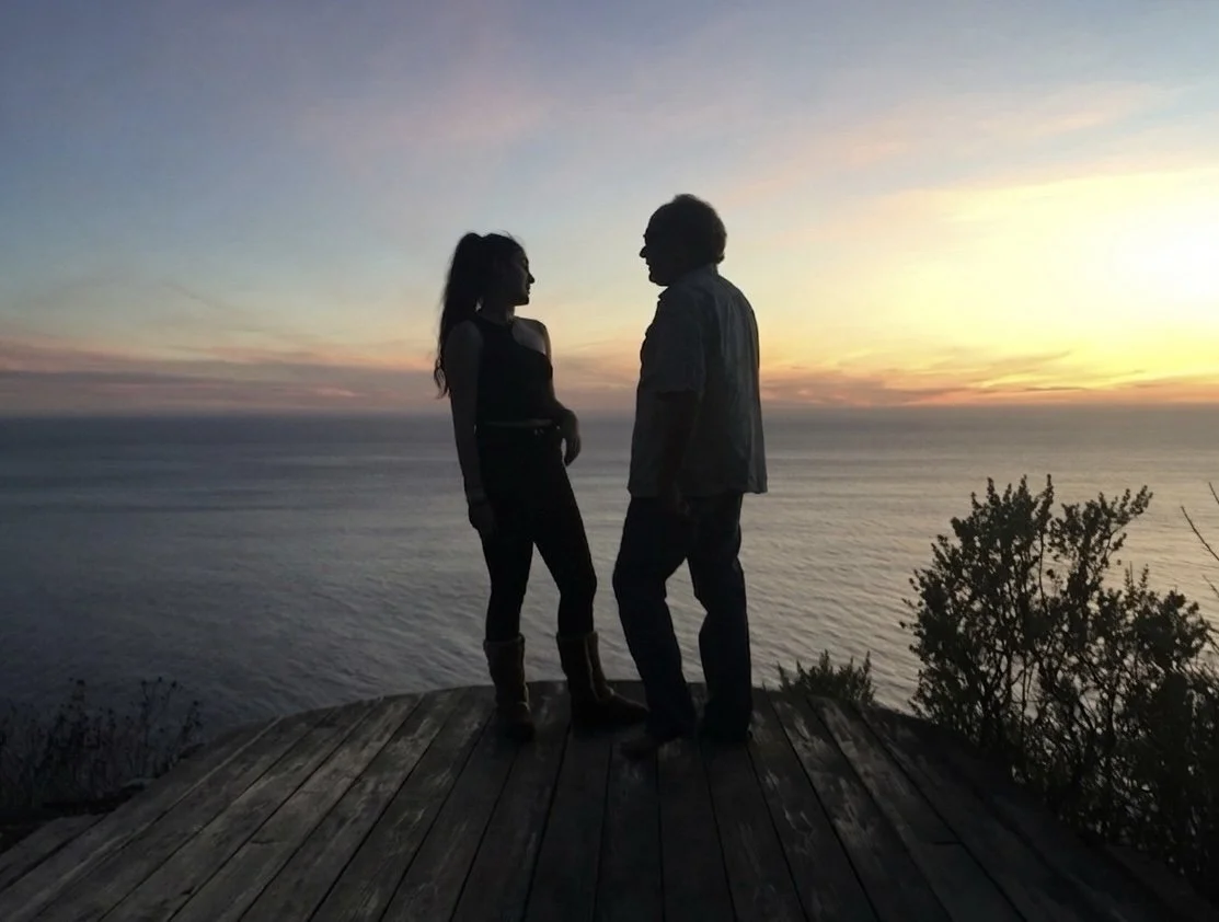 A couple standing in front of a coastal sunset. flip-target