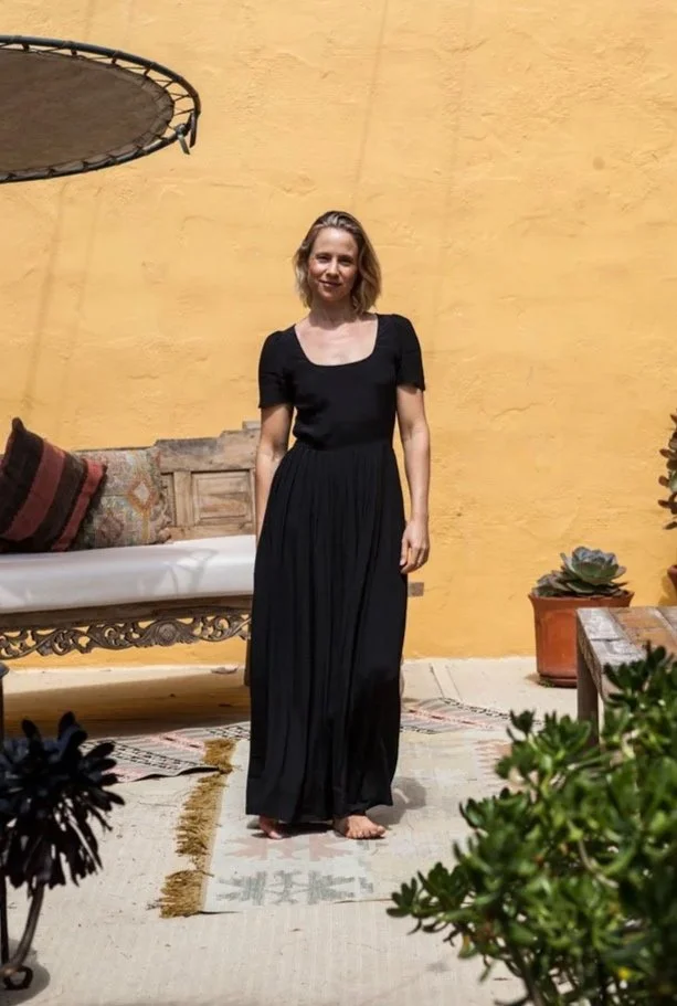 A woman in a black dress standing barefoot on a beige rug in front of a yellow wall. #slideInRight-scroll