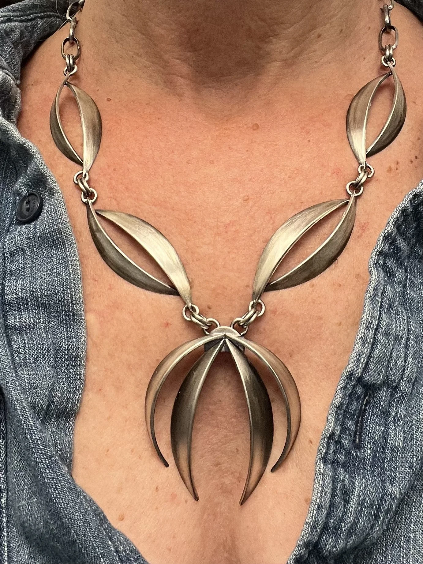 A woman wearing a large sterling silver necklace with leaf-shaped segments.