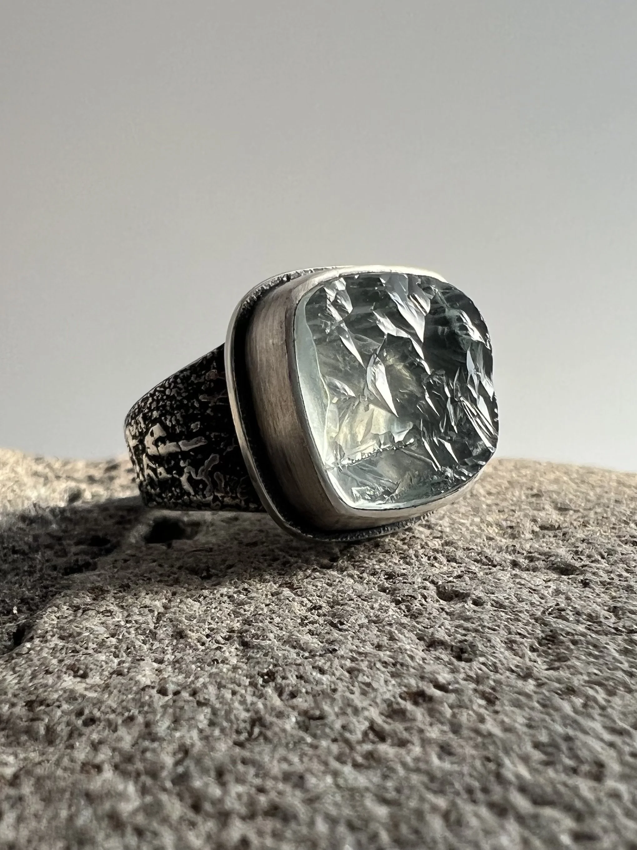 Close-up of a sterling siver ring with aqua marine stone, placed on a textured surface, with a plain background.