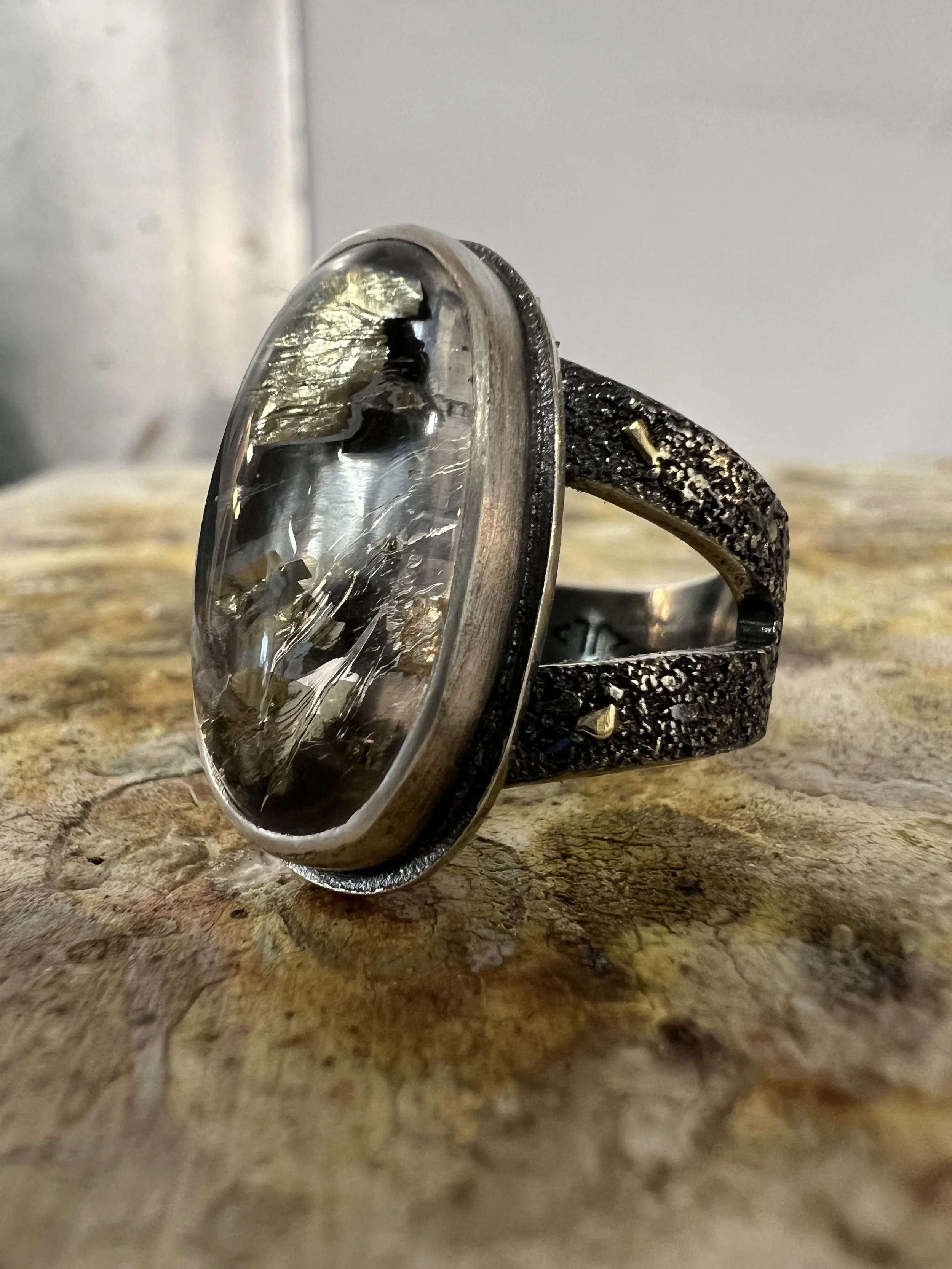A sterling silver ring with an oval clear gemstone set in a textured band is placed on a wooden surface.