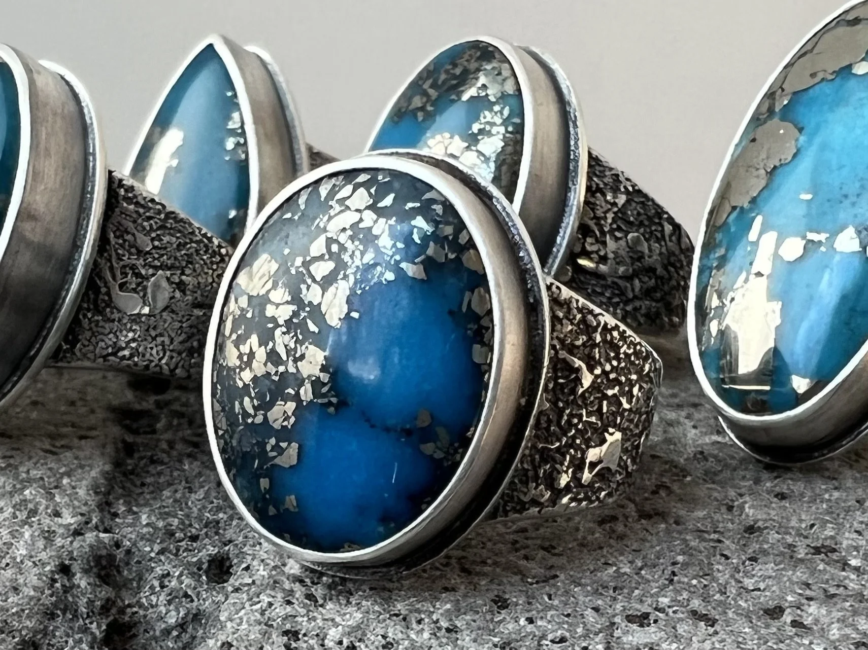 Set of sterling silver rings with turquoise and pyrite on a gray surface.