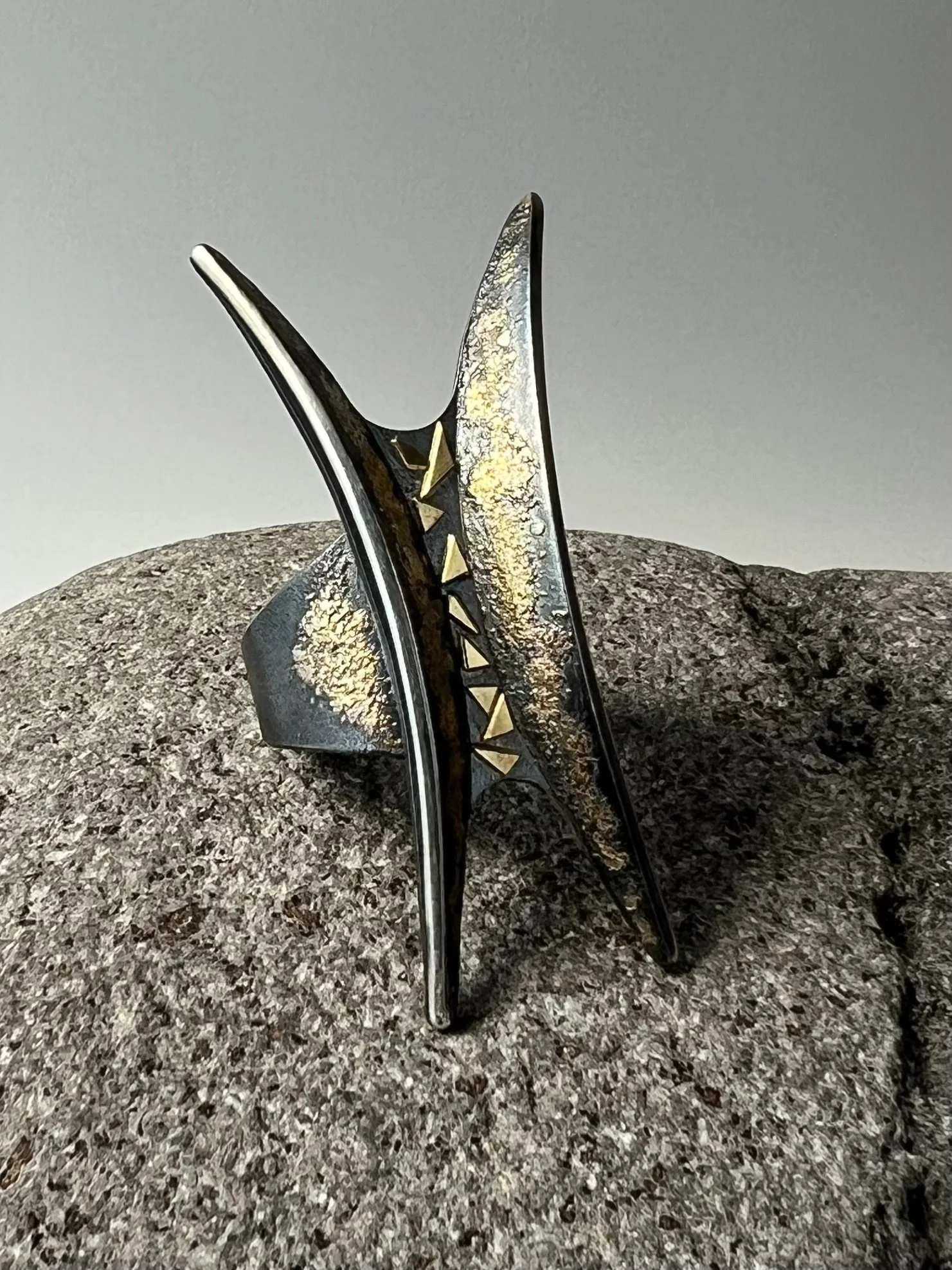 Close-up of an oxidized sterling silver ring with gold accents on a textured surface with a neutral background.