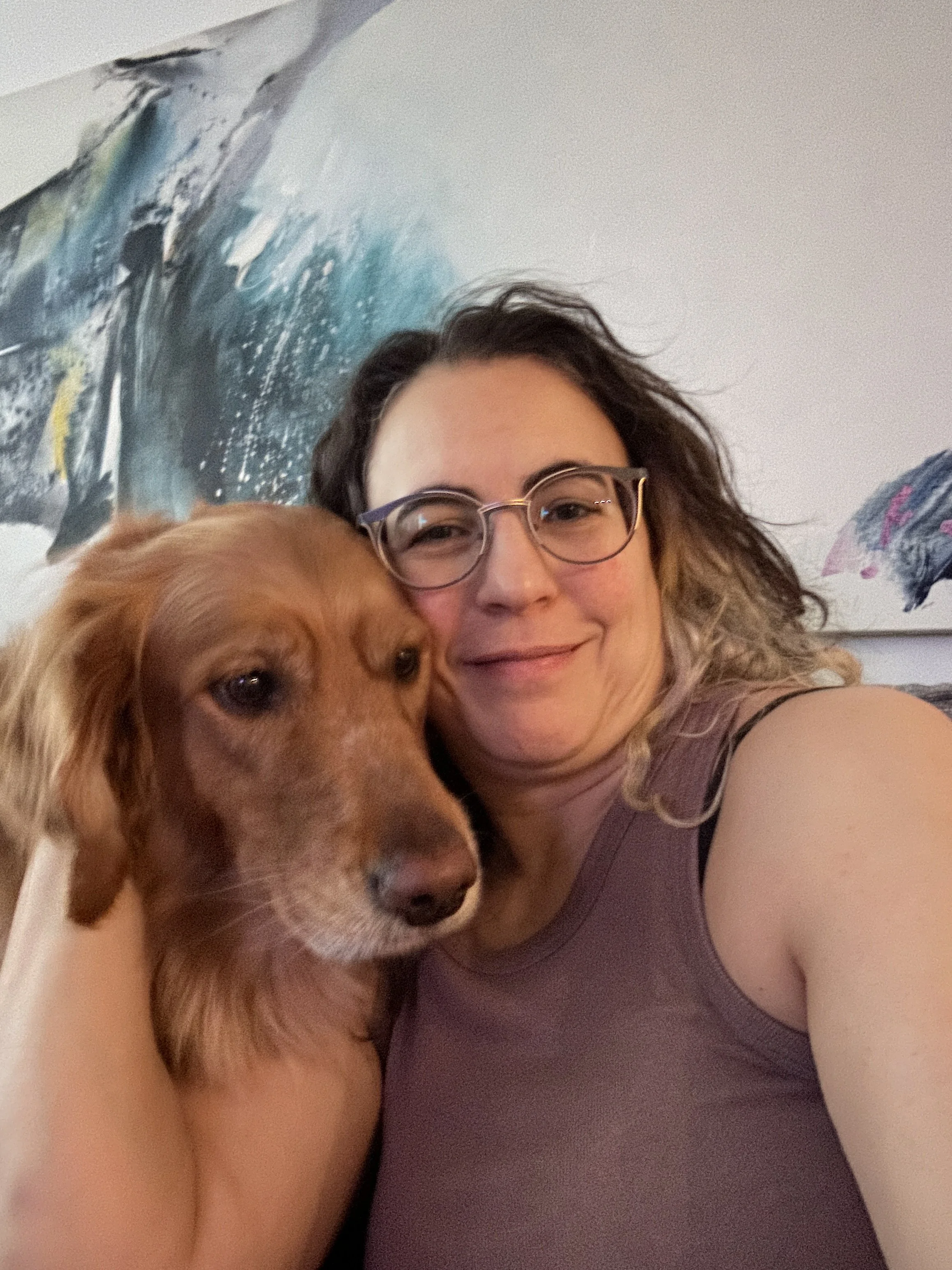 A selfie featuring a Golden Retriever and a woman with brown hair and glasses