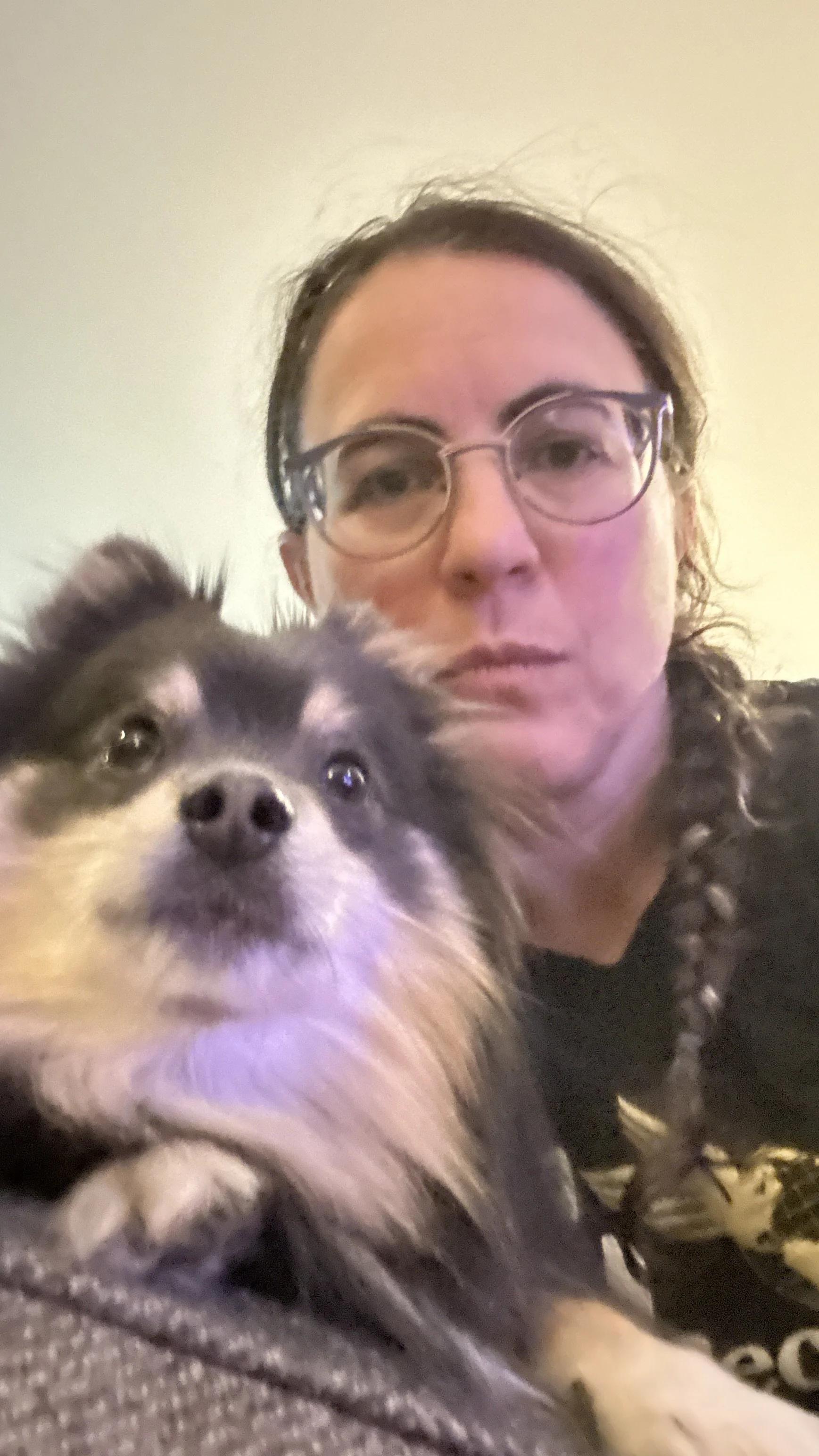 A woman wearing glasses and dark clothing holding a Pomeranian dog with a black, white, and gray coat.