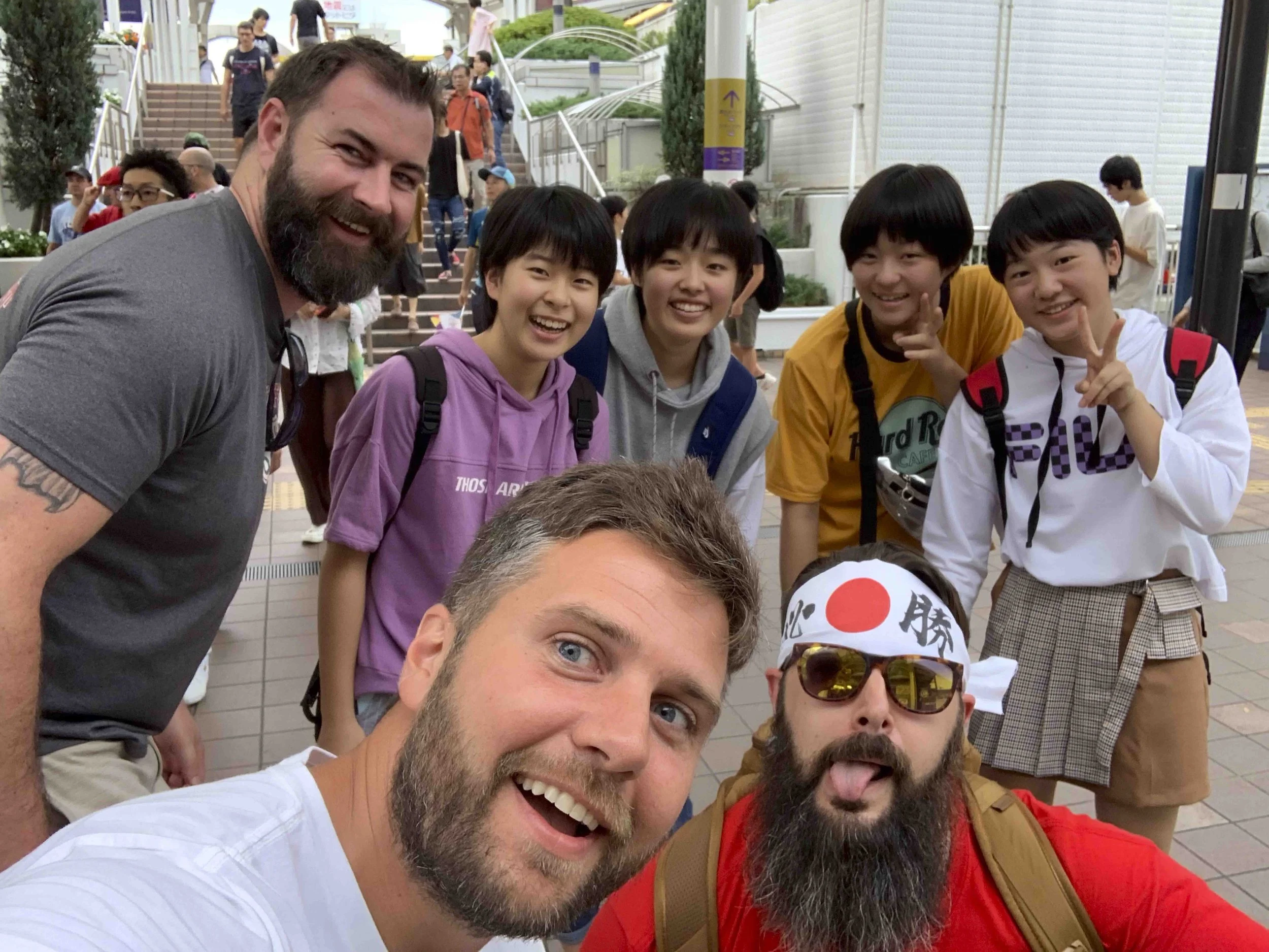A group of diverse people at an outdoor event, smiling and posing for a photo with stairs and other people in the background.