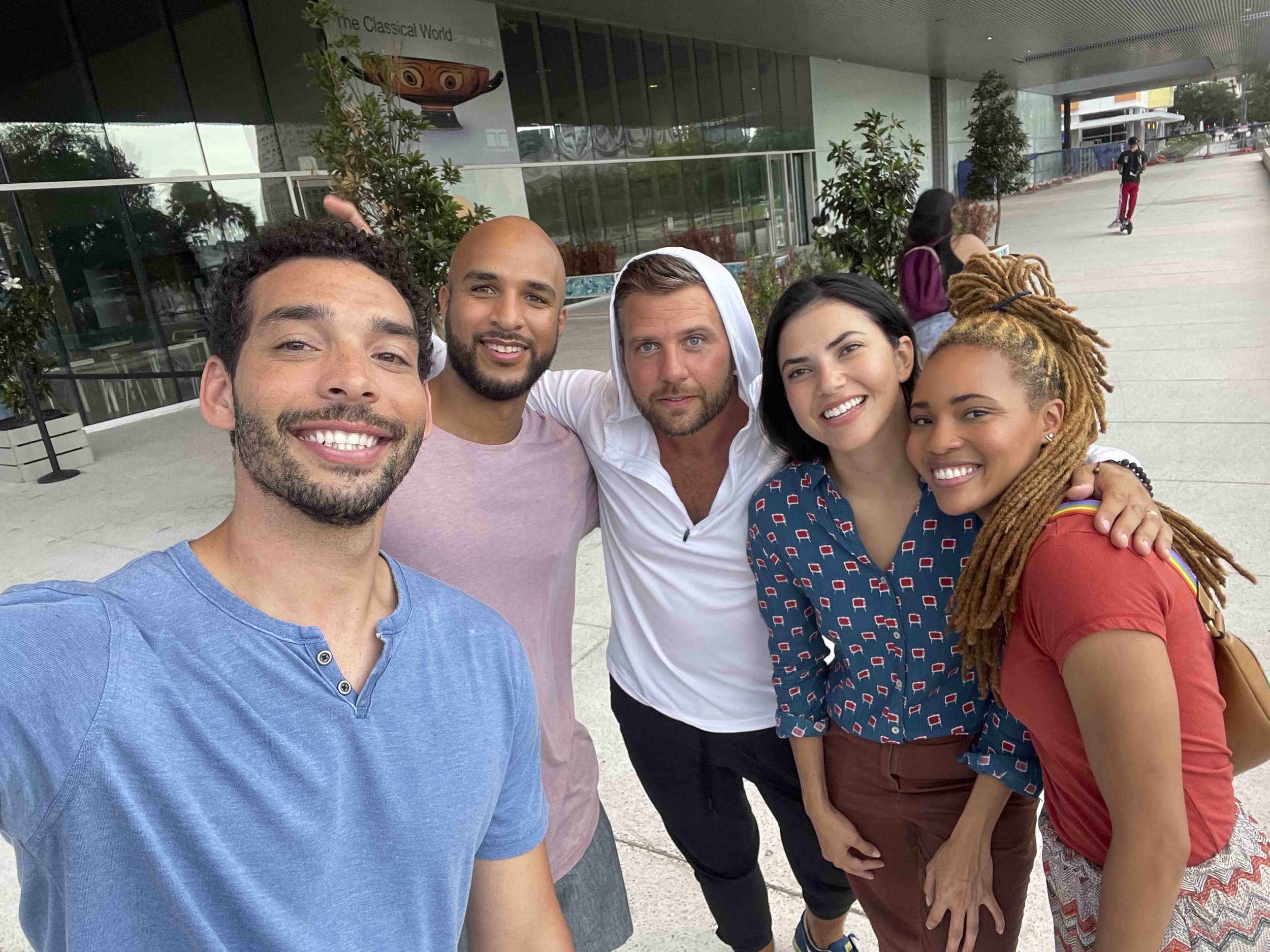 Group of five diverse friends taking a selfie outdoors in an urban setting, smiling and posing together.