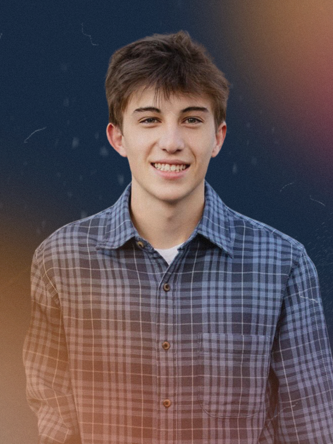 A young man with short brown hair, smiling, wearing a blue checkered button-up shirt, against a dark background.