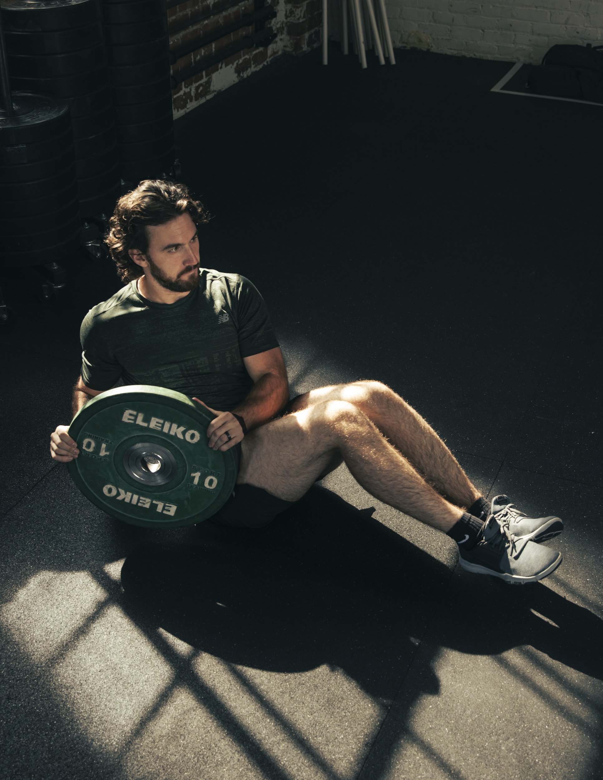 Athletic fitness advertising photography by Bay Area commercial photographer Kaare Iverson.  Man doing russian twists with a weight in a sunbeam through a window in a crossfit gym.
