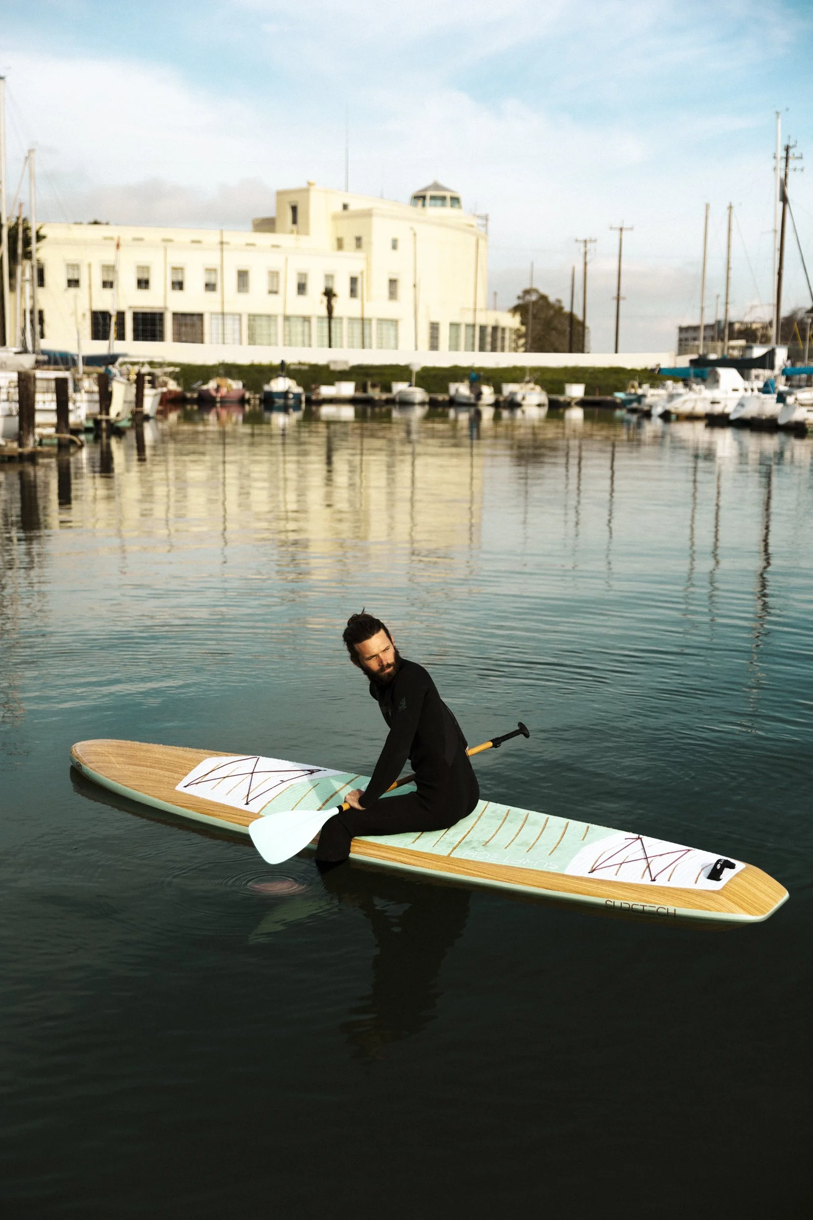Lifestyle photography for San Francisco's Treasure Island Development by California-based commercial photographer Kaare Iverson. Man sitting on a paddleboard in a marina with sailboats docked behind him.