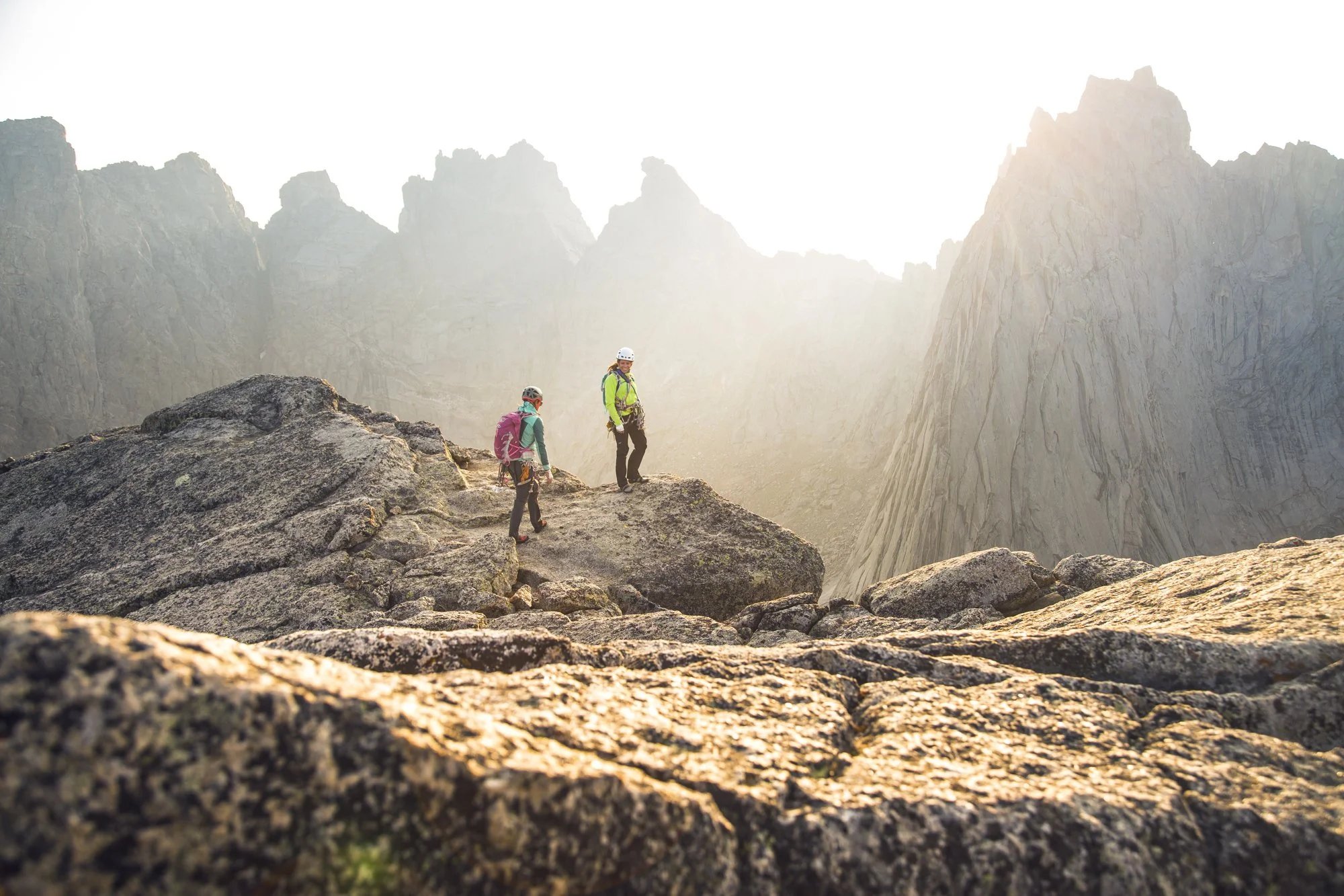 Outdoor adventure and lifestyle image by commercial photographer Kaare Iverson.  Two women summit a mountain in Wyoming at sunset, with steep, jagged mountains in the background.
