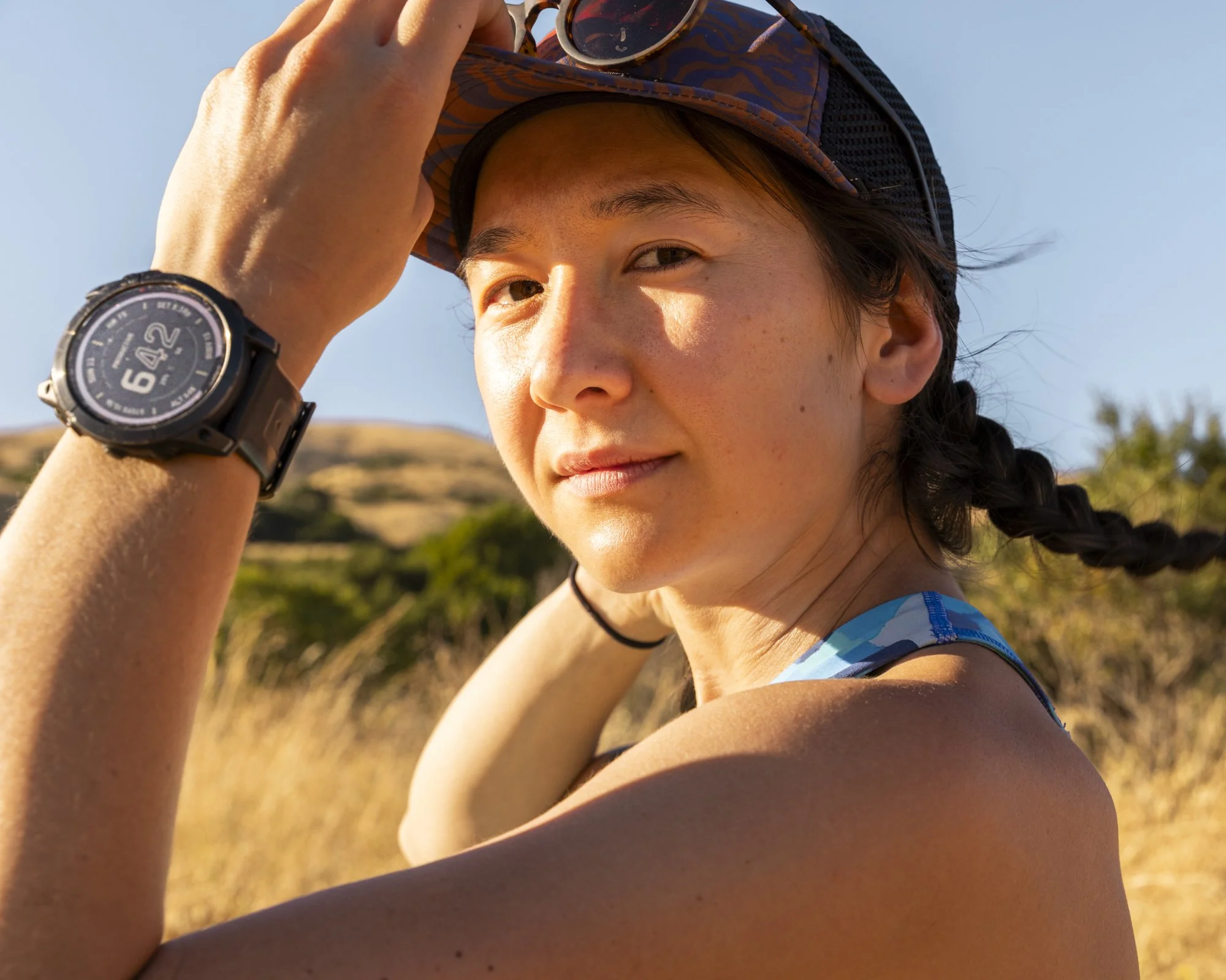 Fitness technology and smartwatch photography by San Francisco Bay Area based commercial photographer Kaare Iverson.  Trail runner adjusts hat while looking at camera with her fitness watch in frame.
