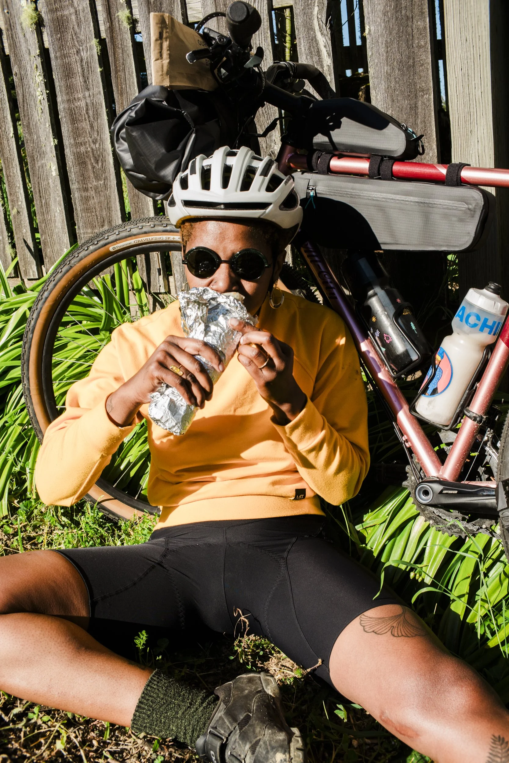 Product lifestyle photography of frame bag kit from Osprey Packs by California commercial photographer Kaare Iverson. Cyclist woman eating a burrito while leaning on her bike in the sun.