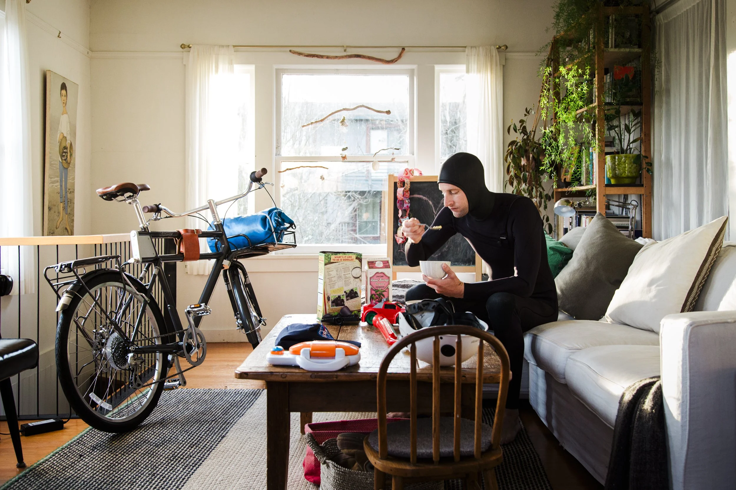 E-Bike detail photography and lifestyle image for PON Bikes shot in California by Kaare Iverson.  Surprising and unique image of a man in a wetsuit eating cereal before leaving to surf with his bike which is charging in living room.