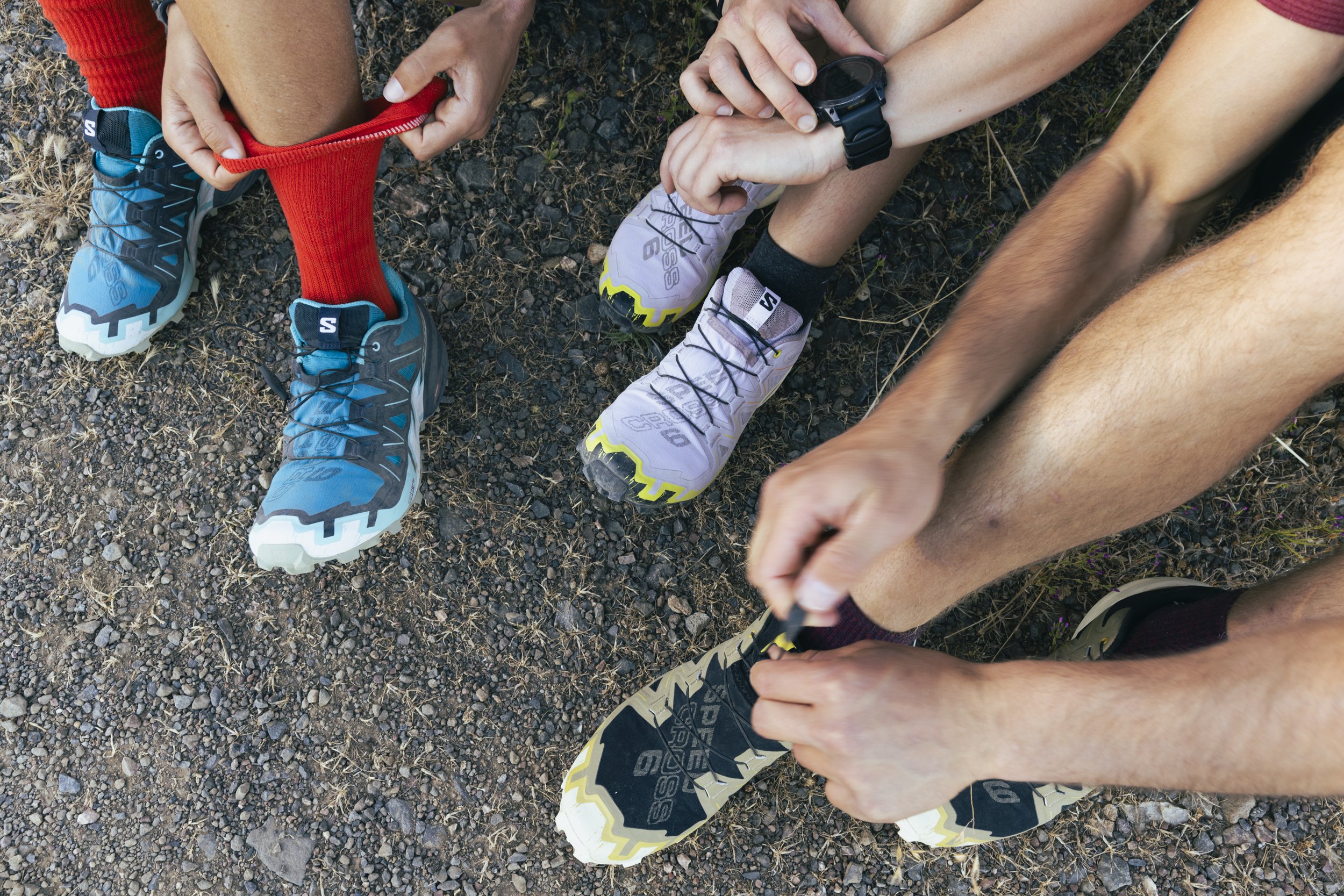 Athletic wear fitness lifestyle photography by San Francisco based photographer Kaare Iverson. Close-up of three runners in athletic gear and Salomon shoes adjusting their socks on a rocky outdoor trail.