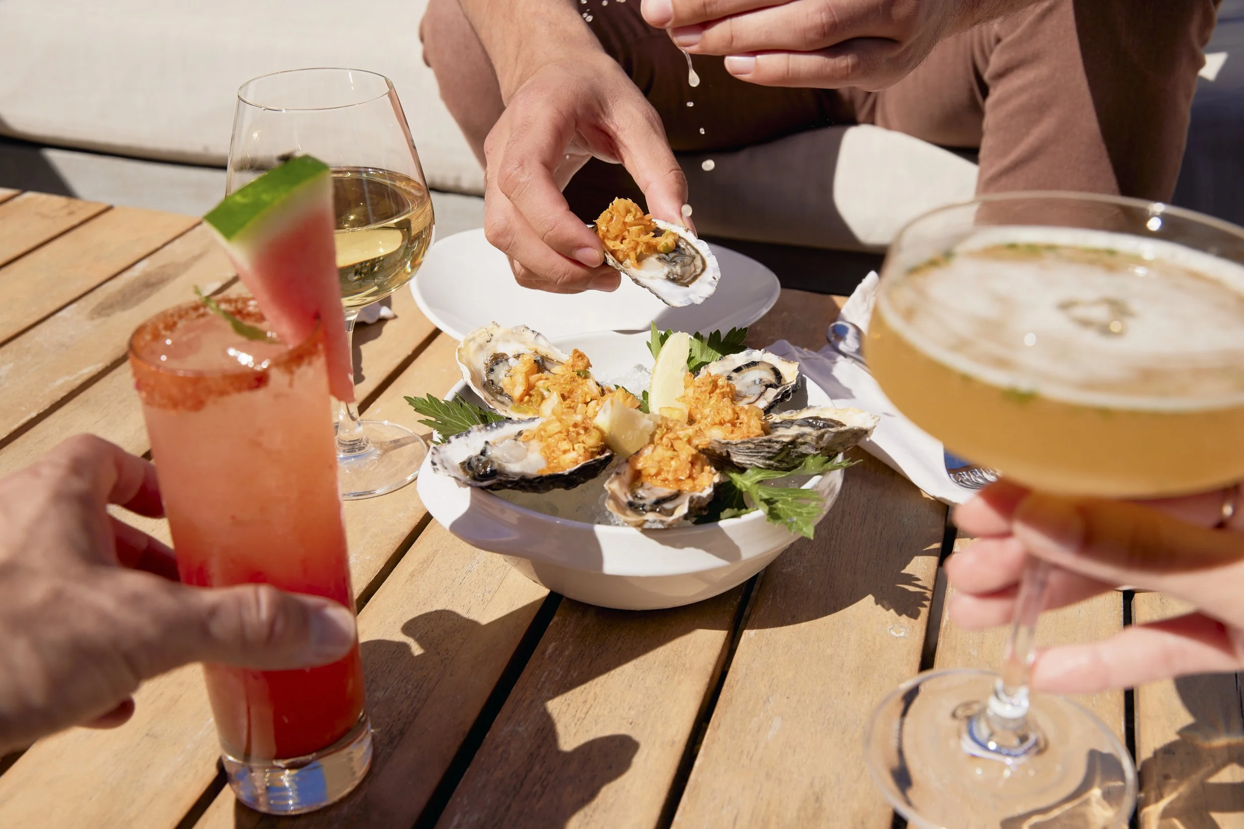 Immersive POV of people enjoying beverages and oysters on a wooden table at an outdoor setting.  Shot by commercial lifestyle photographer Kaare Iverson in California for Treasure Island Development Group.