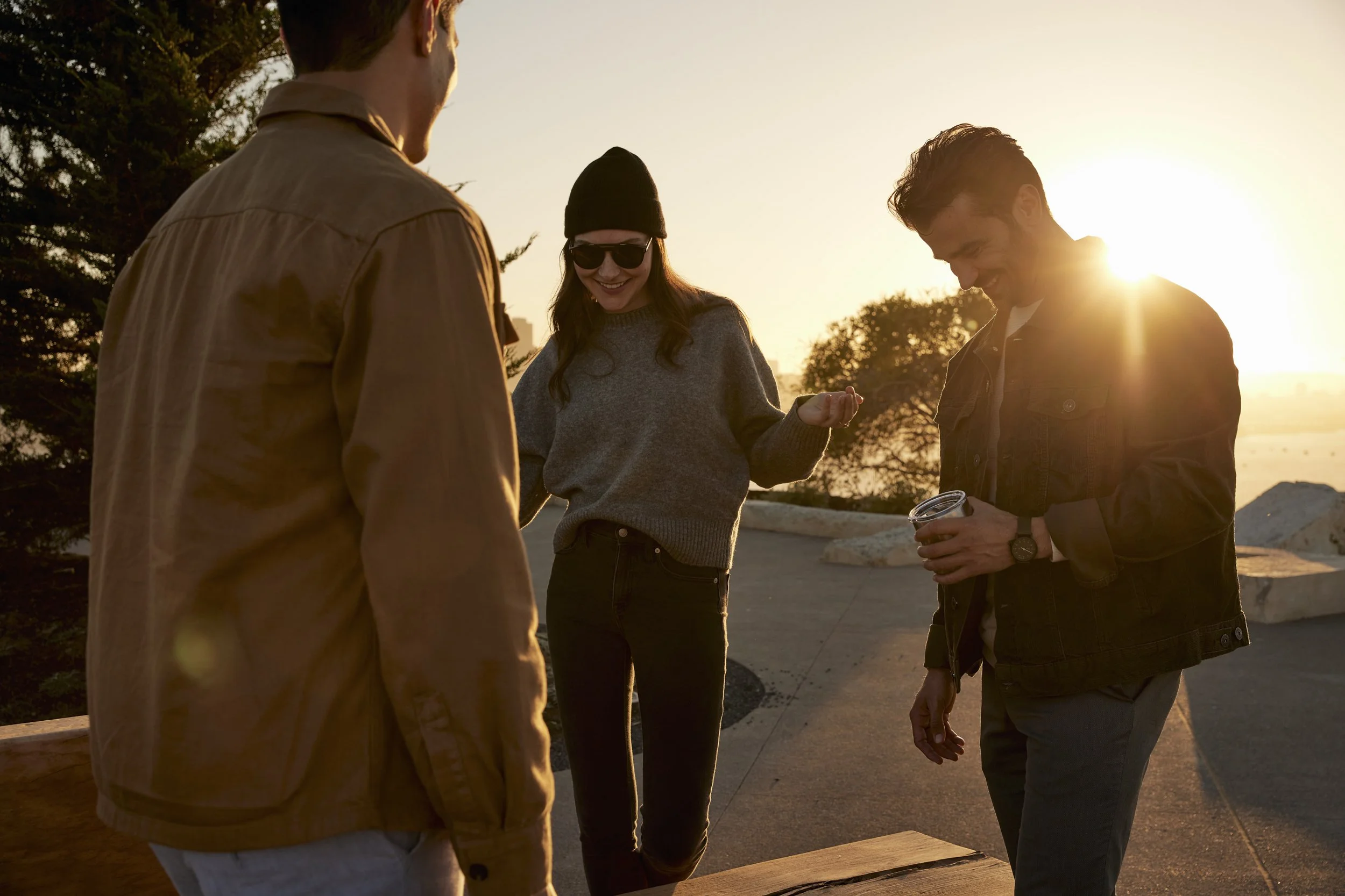Urban young adult lifestyle photography by commercial photographer Kaare Iverson. Four young adults standing outdoors during sunset, smiling and engaging with each other. One person is holding a bottle of wine.  Shot in California for Treasure Island