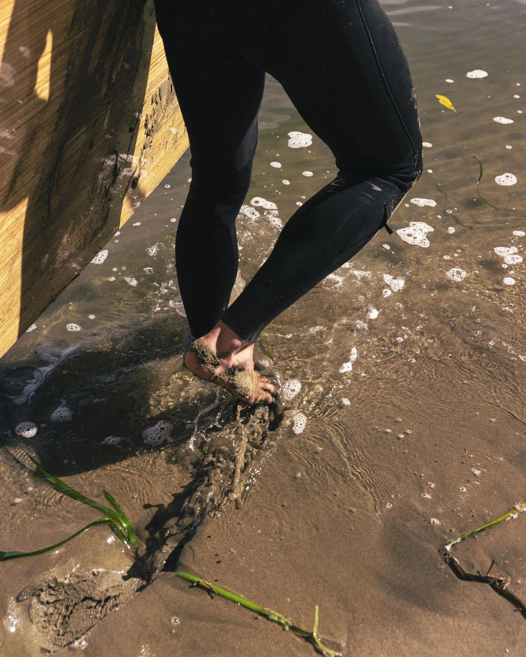 Lifestyle photography for San Francisco's Treasure Island Development by California-based commercial photographer Kaare Iverson. A person in a wetsuit stepping on wet sand at the water's edge of Clipper Cove.