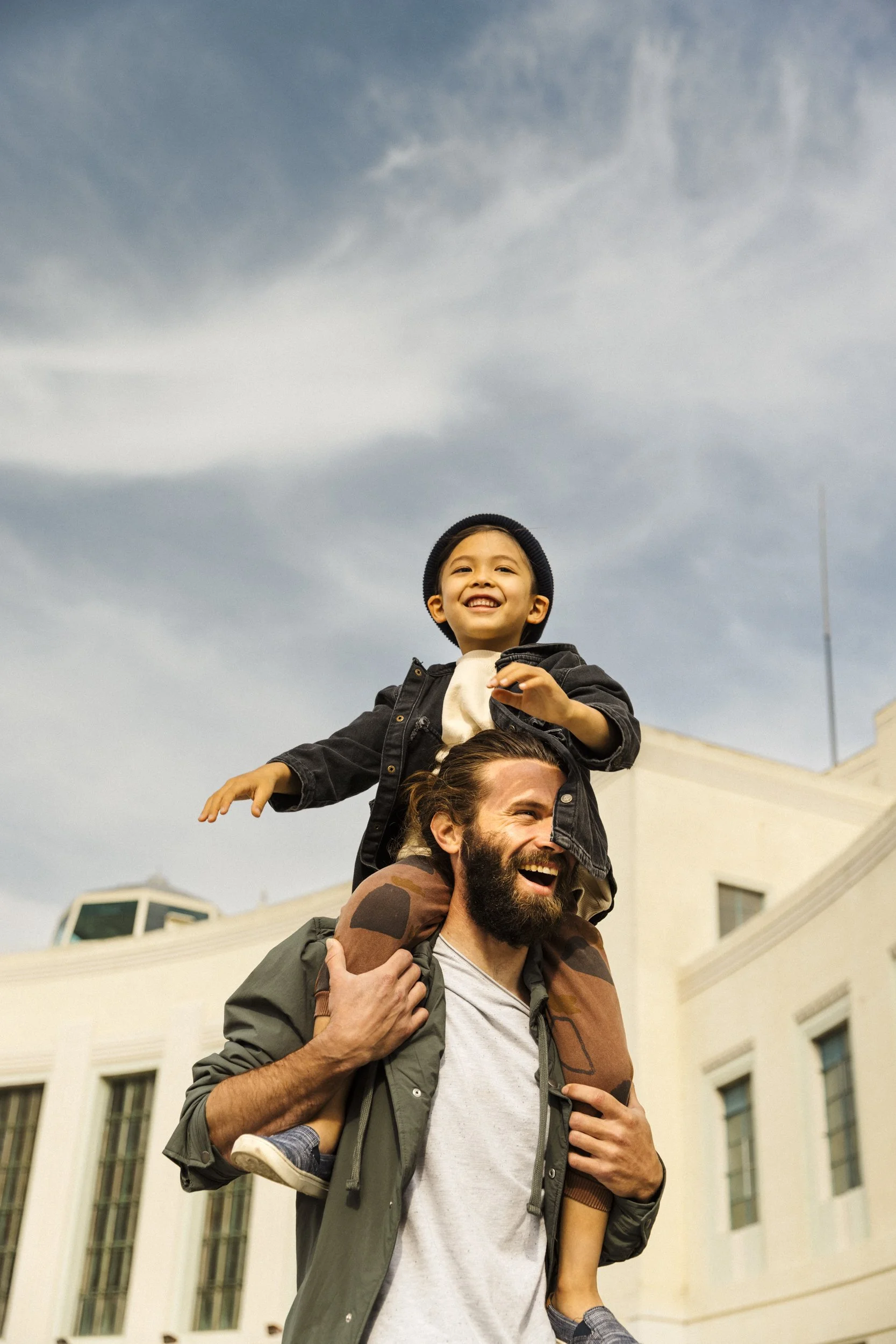 A man carrying a smiley child on his shoulders outside near Building B on Treasure Island In San Francisco.  Shot by commercial photographer Kaare Iverson for a California based lifestyle advertising campaign for development and real estate