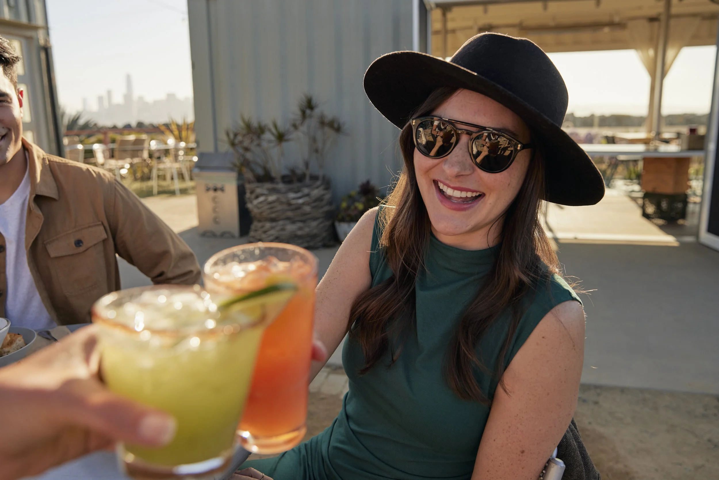 Immersive POV of woman cheersing beverages at sunset at MerSea restaurant on Treasure Island. Shot by commercial lifestyle photographer Kaare Iverson in California's Bay Area.