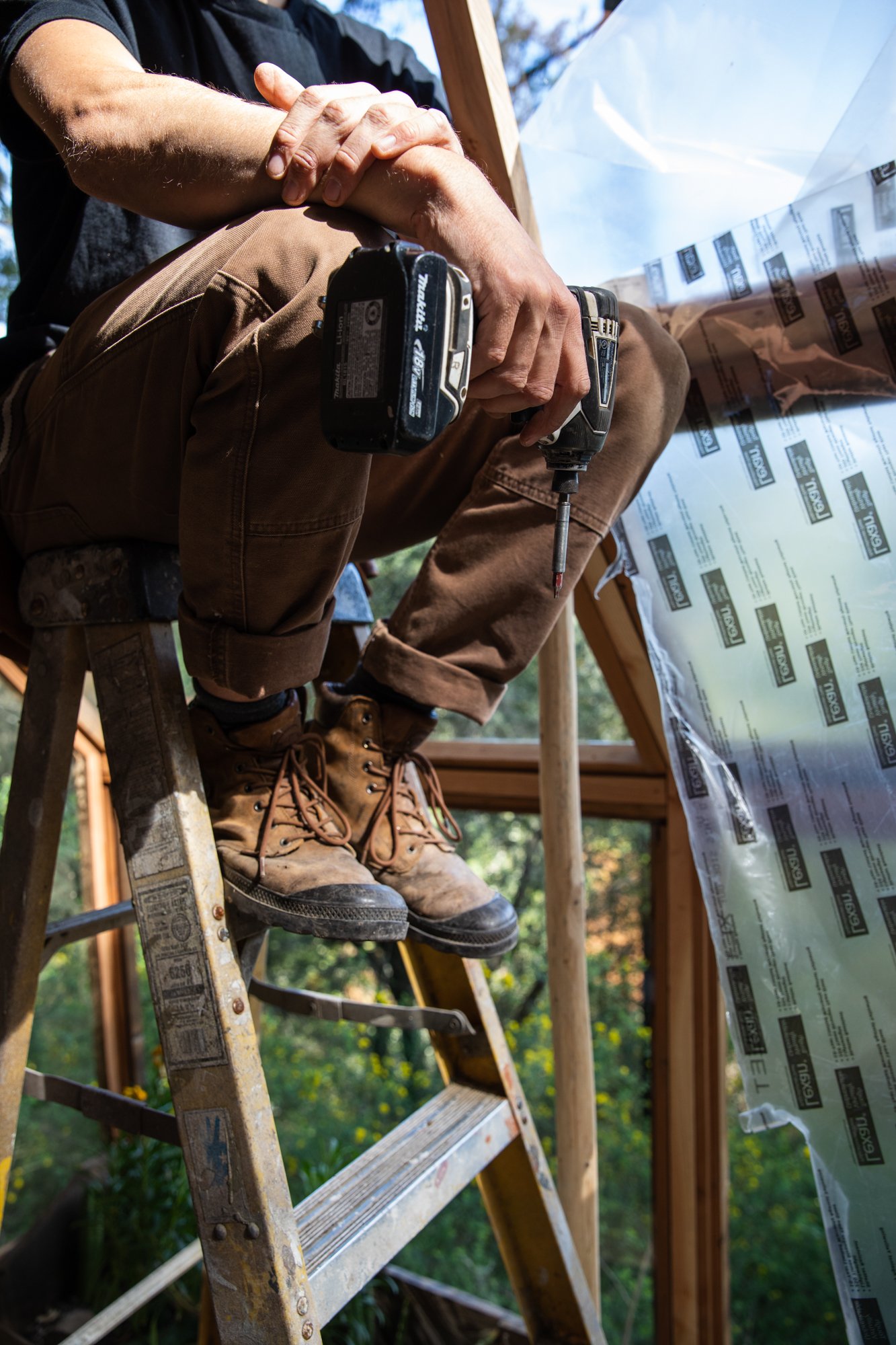 Image from PRAXIS, a photo essay shot in California by photographer Kaare Iverson. A person working on a construction project, standing on a ladder, using a drill, with a wooden structure visible in a bright outdoor setting.