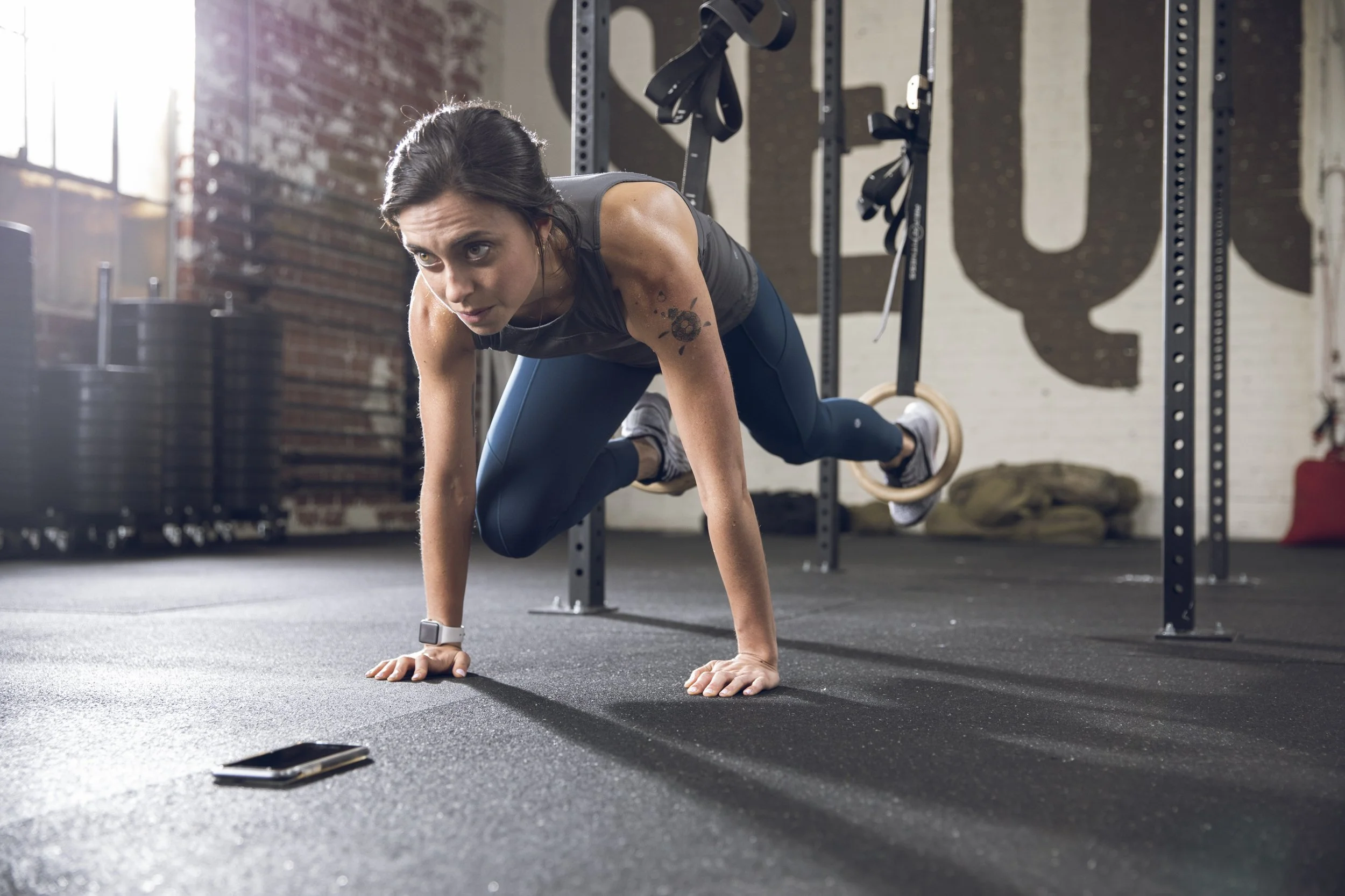 Athletic fitness and training photography by Bay Area commercial photographer Kaare Iverson. A woman with dark hair doing a plank exercise on a black gym mat in a CrossFit gym. She is wearing an Apple Watch. Shot for Future Fit App.