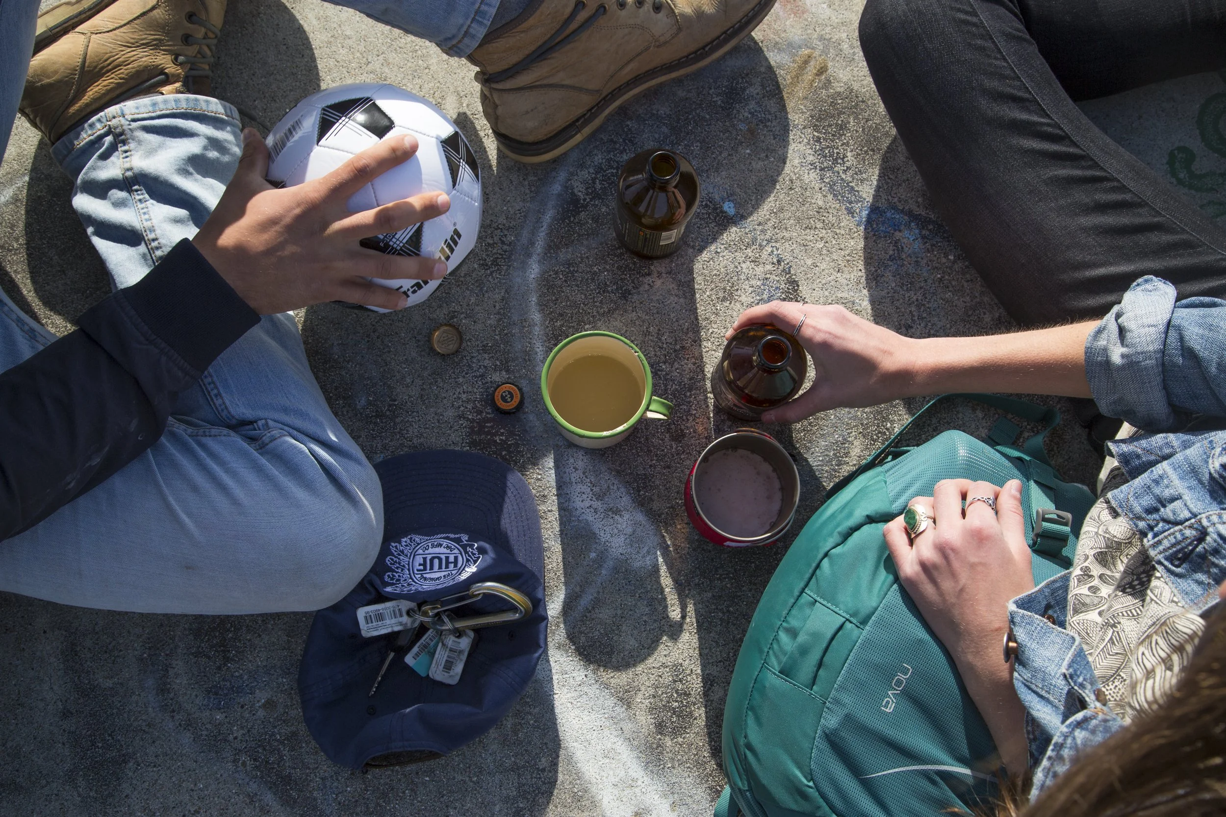 Shot by California commercial photographer Kaare Iverson. Overhead view of people sitting on the ground outdoors, with a soccer ball, drinks, Osprey brand backpack, and some jackets around them.
