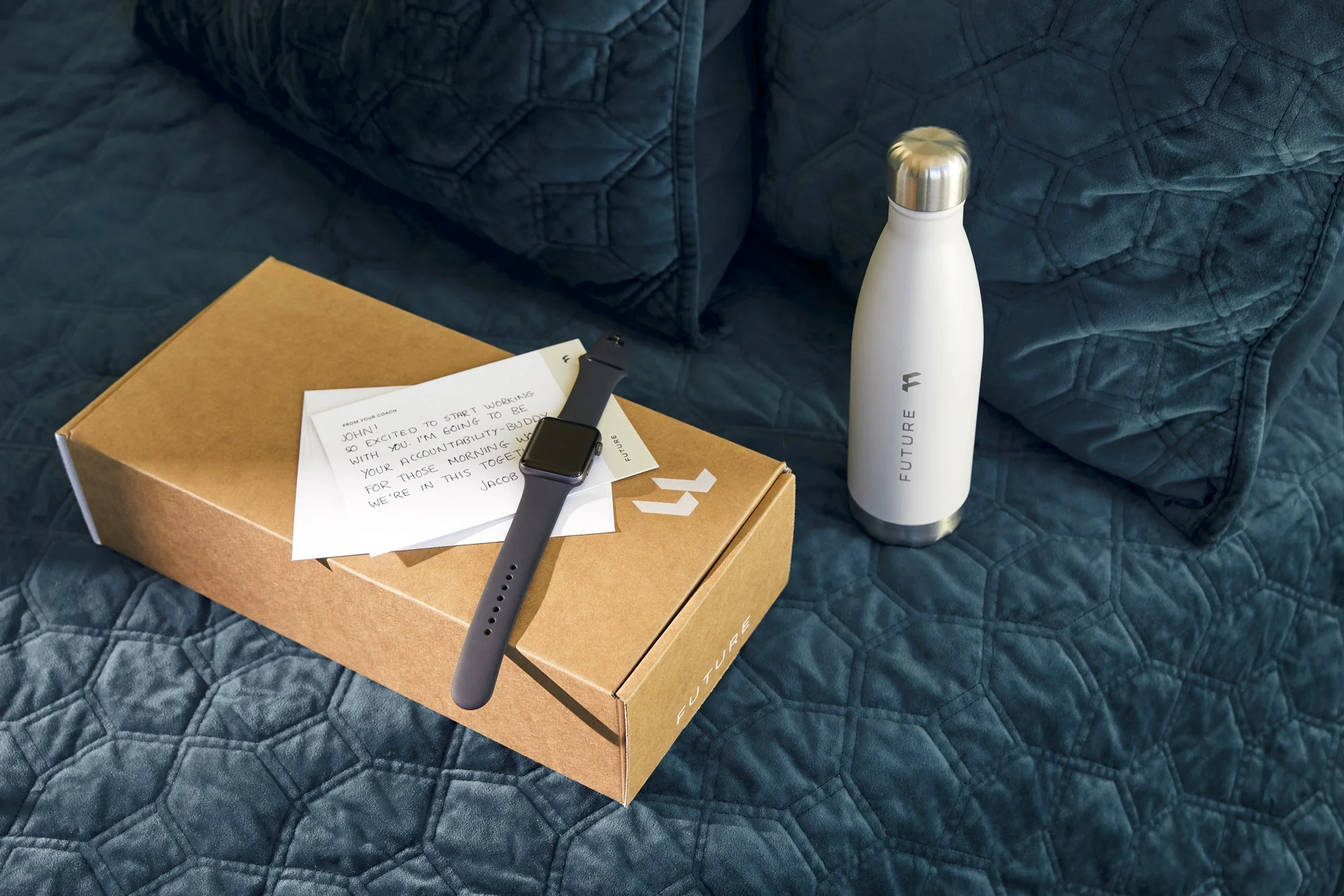 Technology and subscription photography by California commercial photographer Kaare Iverson. Product lifestyle Future welcome kits featuring smartwatch, waterbottle, and personalized note from trainer on a blue bedspread.