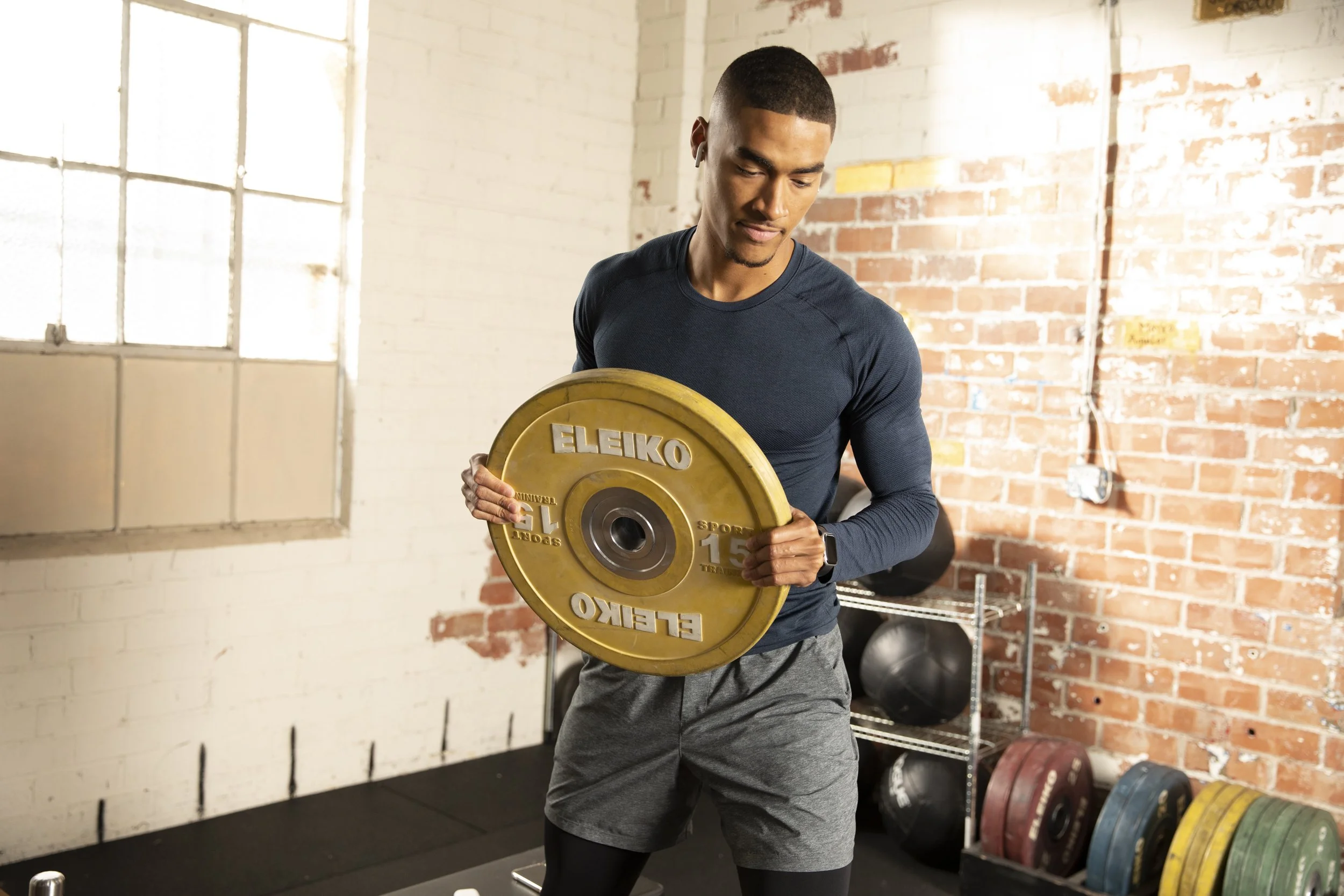 Athletic fitness and training photography by Bay Area commercial photographer Kaare Iverson for Future Fit App. A young man with short hair and gymwear is lifting a weight plate during a workout in a gym with exposed brick walls and large windows.