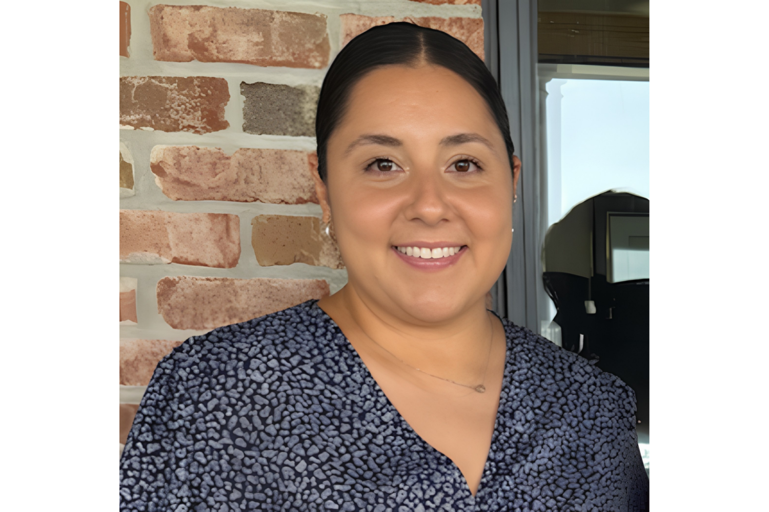 Founder of Communication Therapy & Connection smiling, wearing a dark patterned top, standing in front of a brick wall.