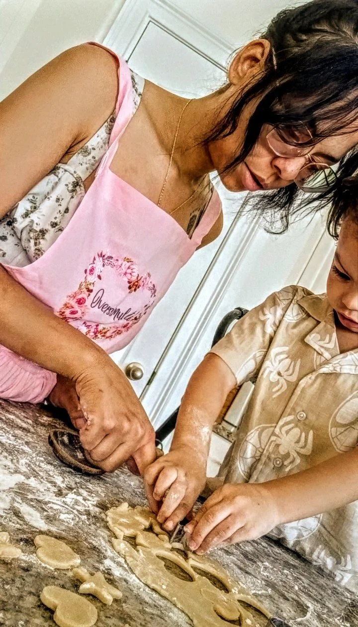 A woman and a child baking cookies together on a kitchen counter, using cookie cutters to cut out shapes from rolled dough.