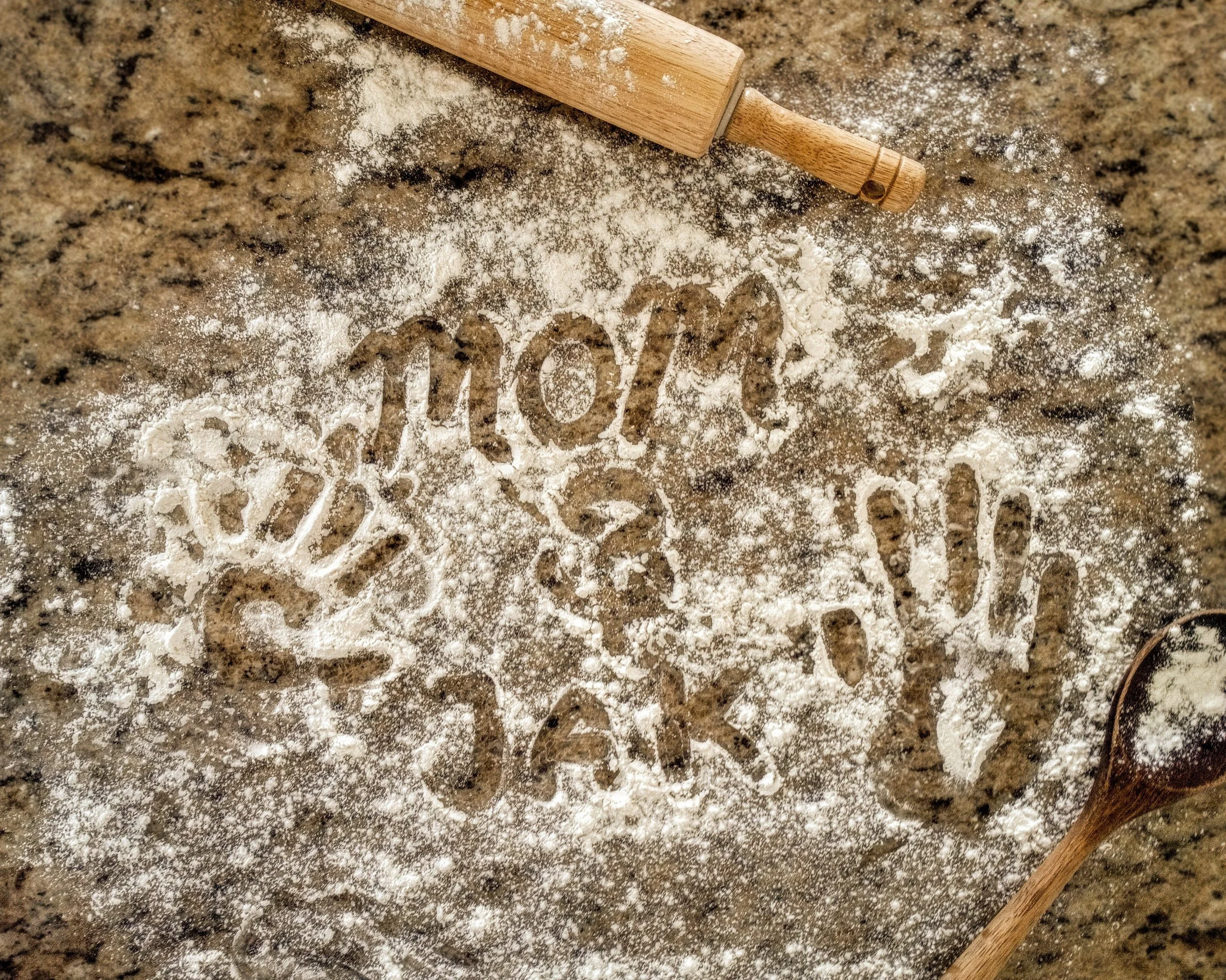 A rolling pin lying on a granite countertop with flour dusted around it and the word 'love' written in the flour.