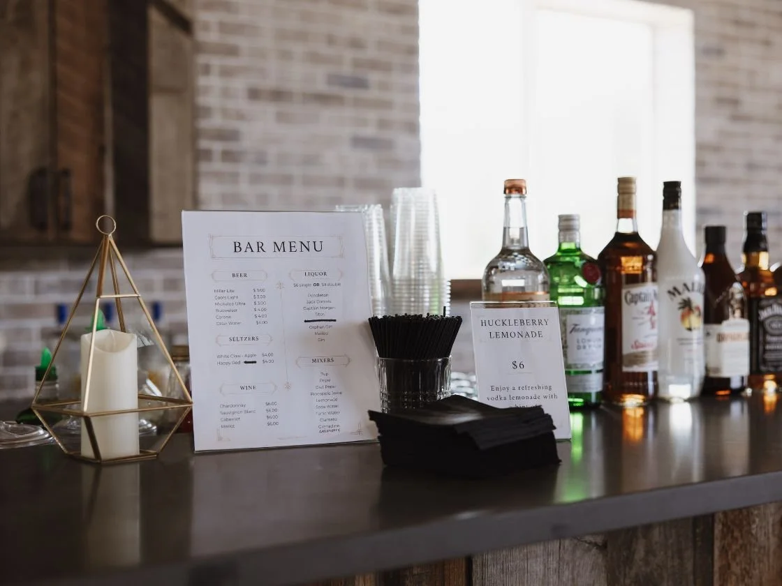 Bar counter with bar menu, black napkins, liquor bottles, cups, and a decorative candle holder