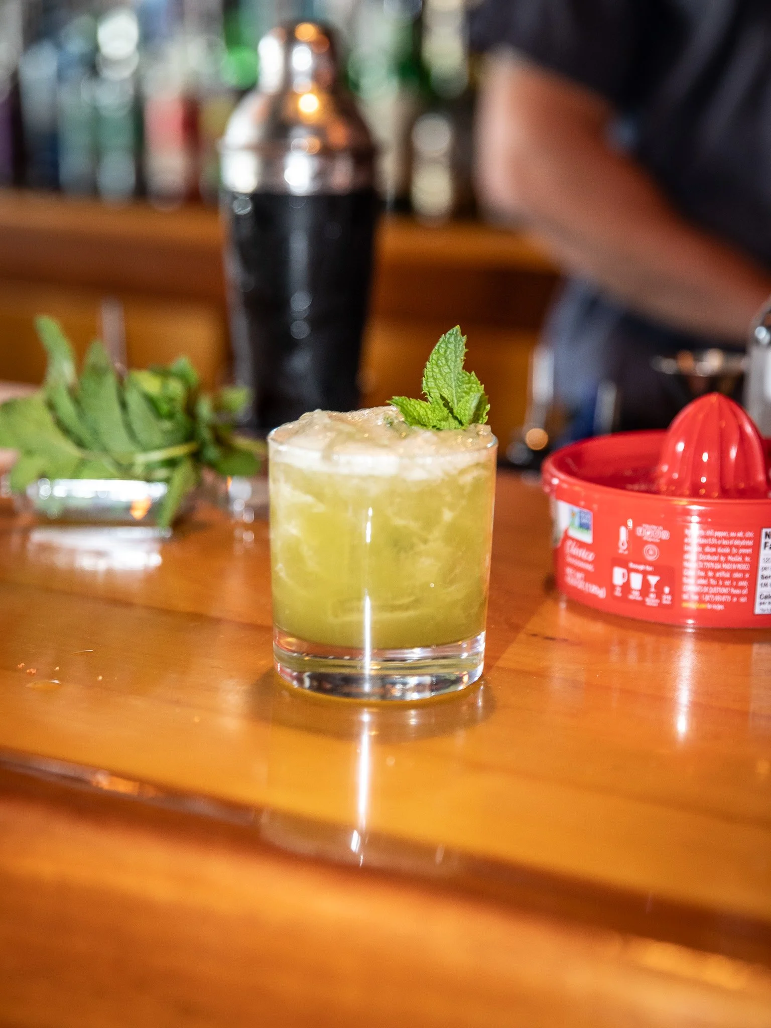 A close-up of a cocktail garnished with a sprig of fresh mint, placed on a wooden surface.