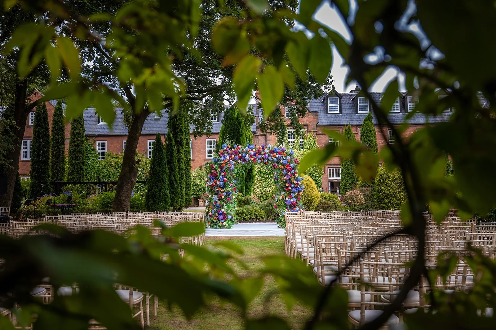 Outdoor ceremony setup with colourful floral arch in Nunsmere Hall Italian gardens
